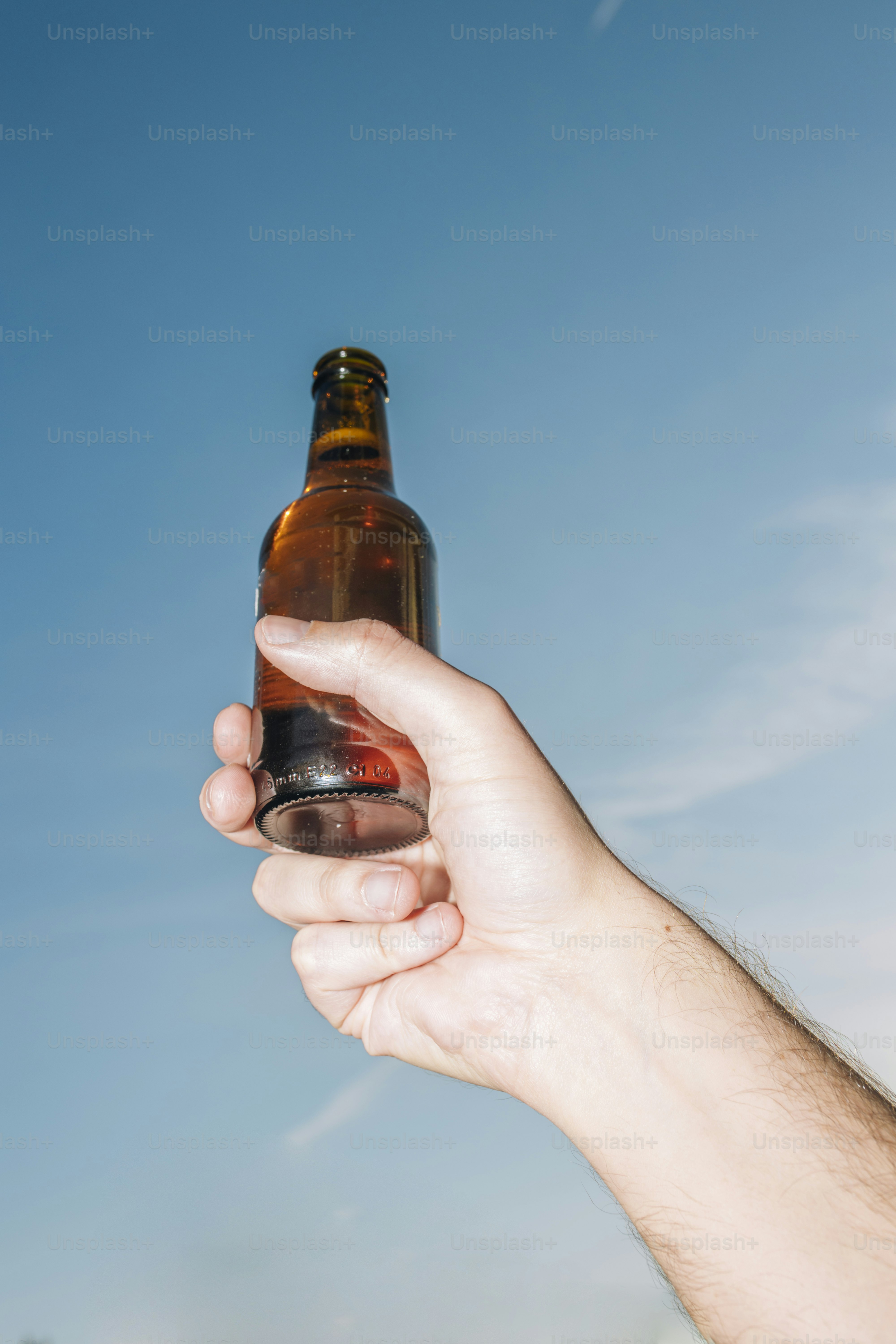 Mão segurando uma garrafa de cerveja de vidro marrom contra o céu azul