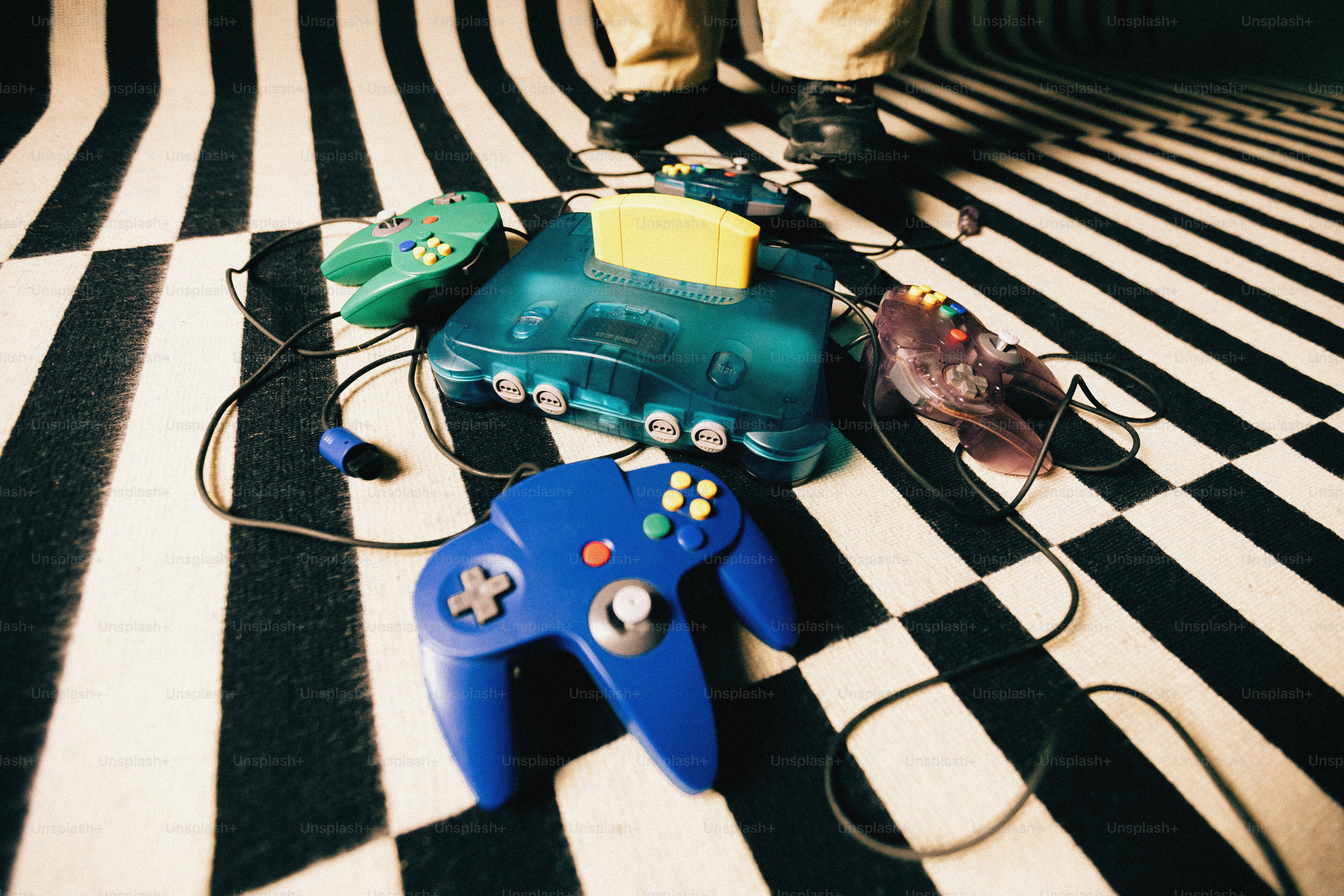 Consola de videojuegos retro con mandos sobre suelo a rayas