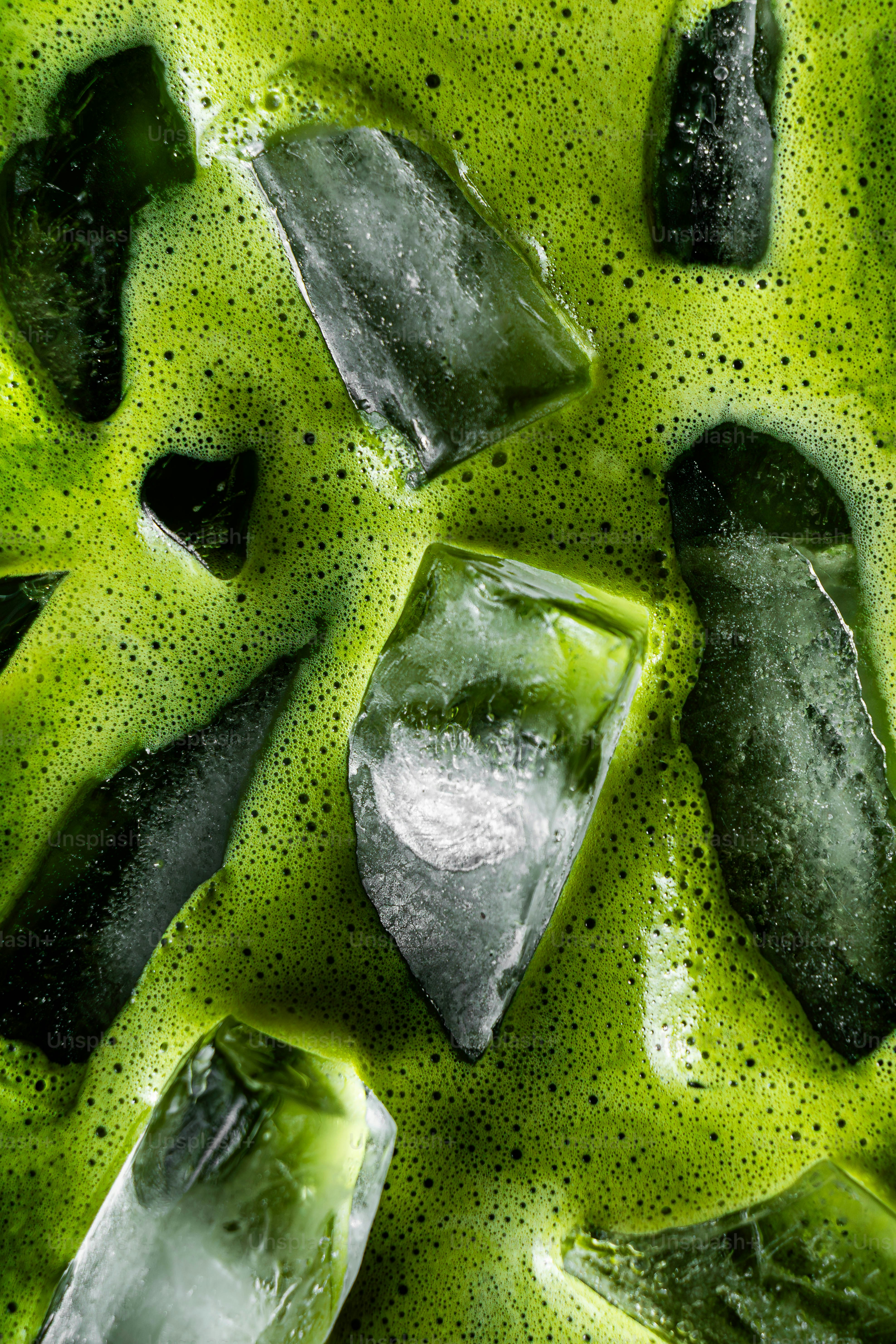 鮮やかな緑色の抹茶ドリンクの中の氷のクローズアップ。