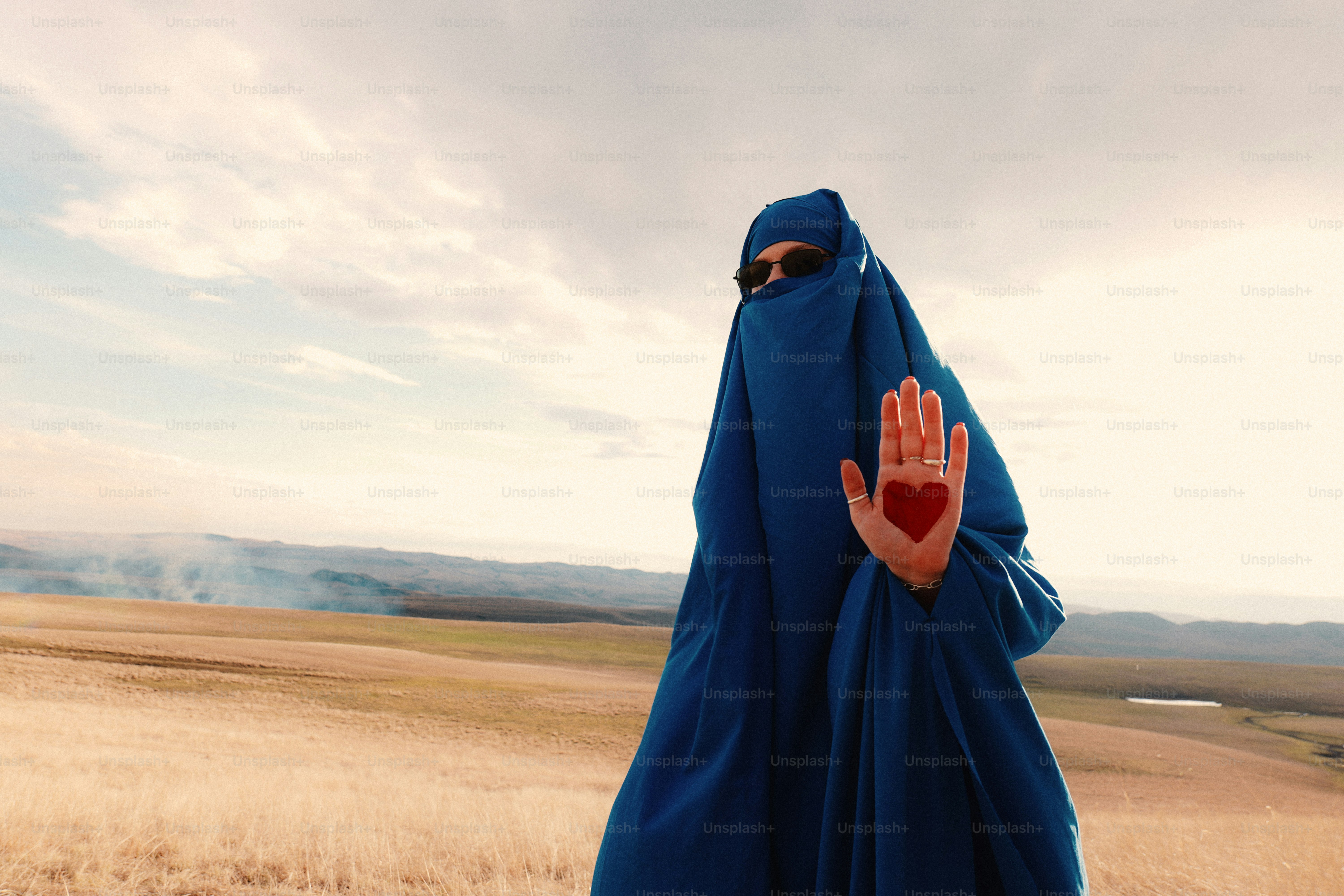 Woman in blue burqa holds hand up with heart