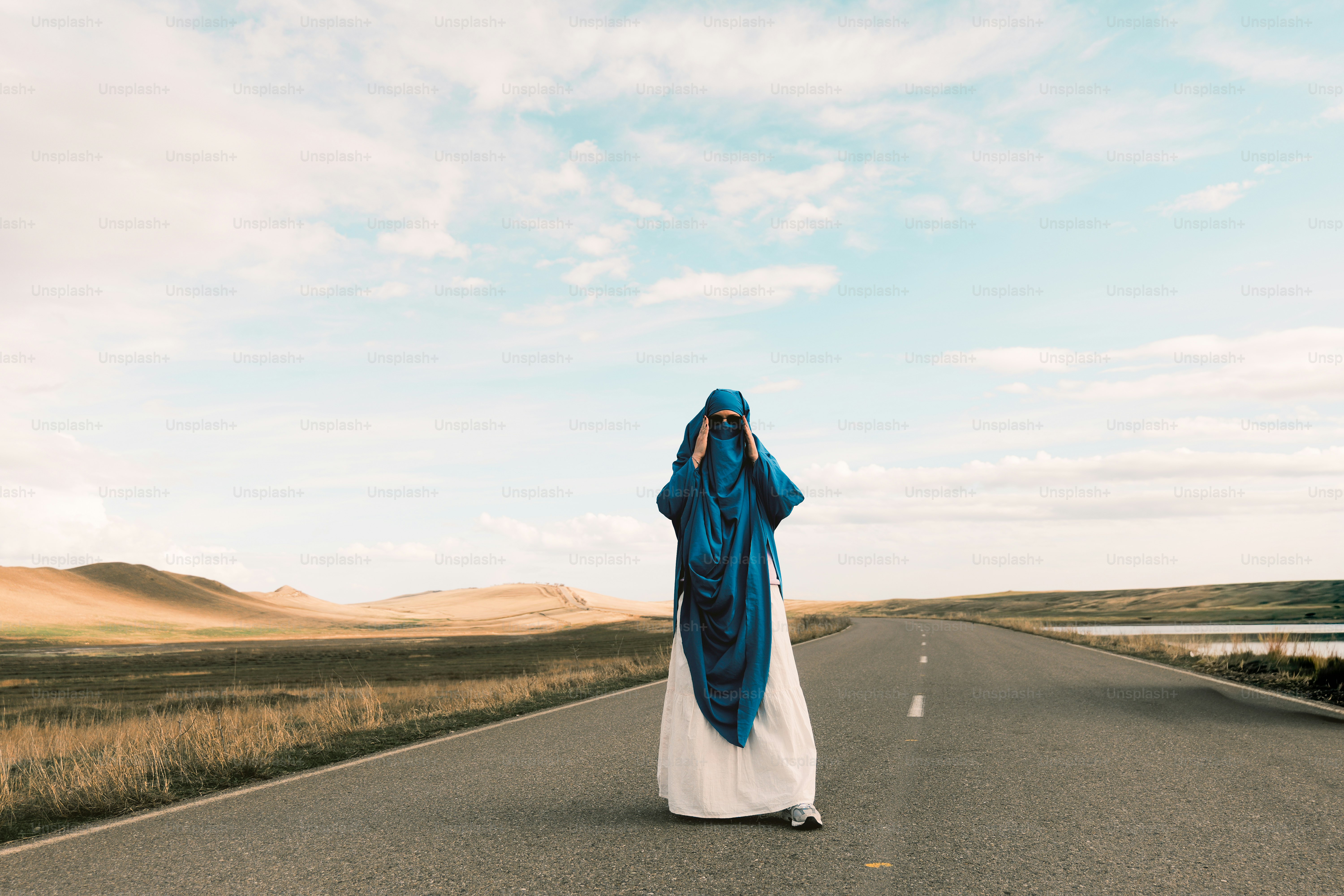 Wanita berburqa biru berjalan di jalan gurun kosong