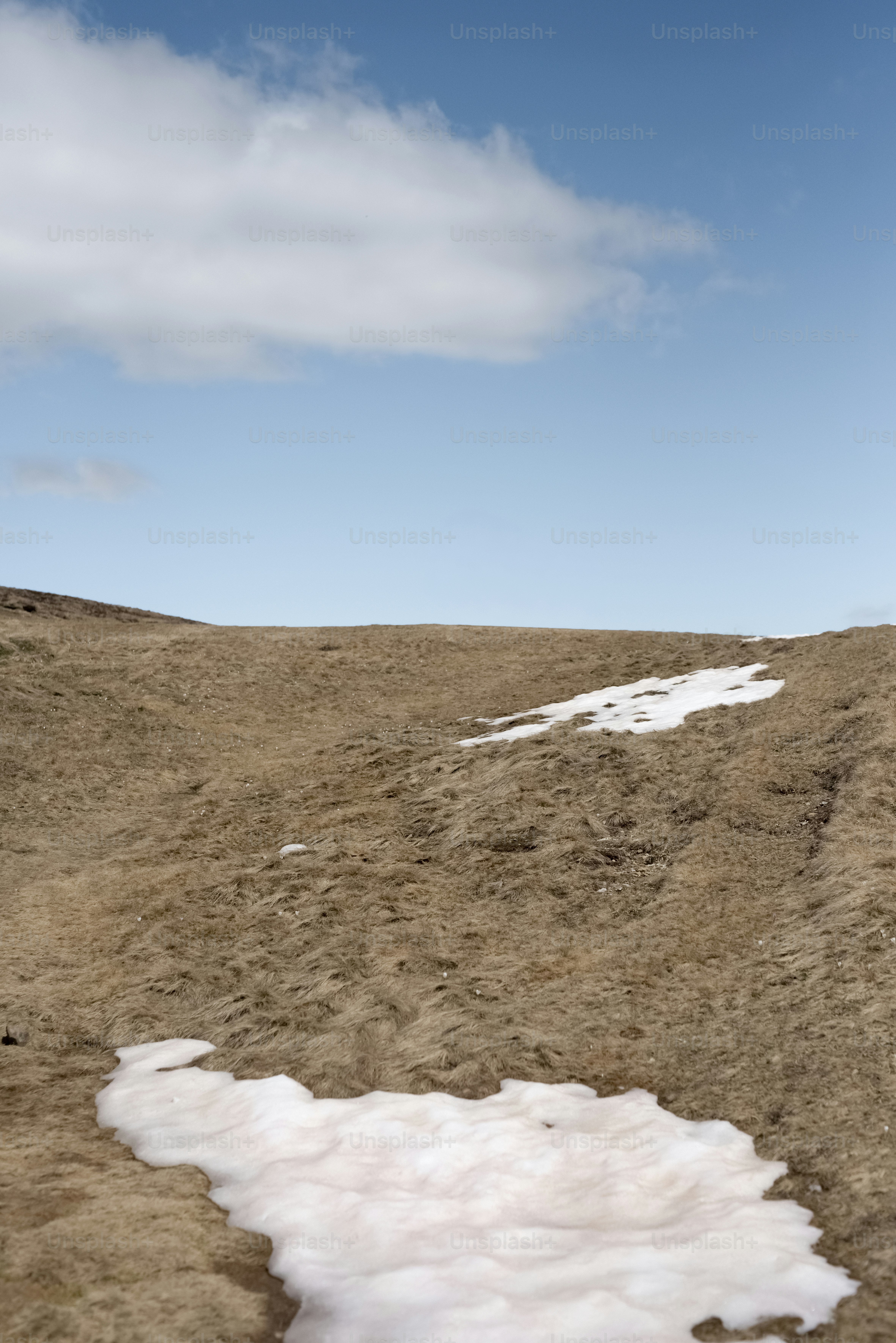 푸른 하늘 아래 눈이 흩어진 갈색 언덕들