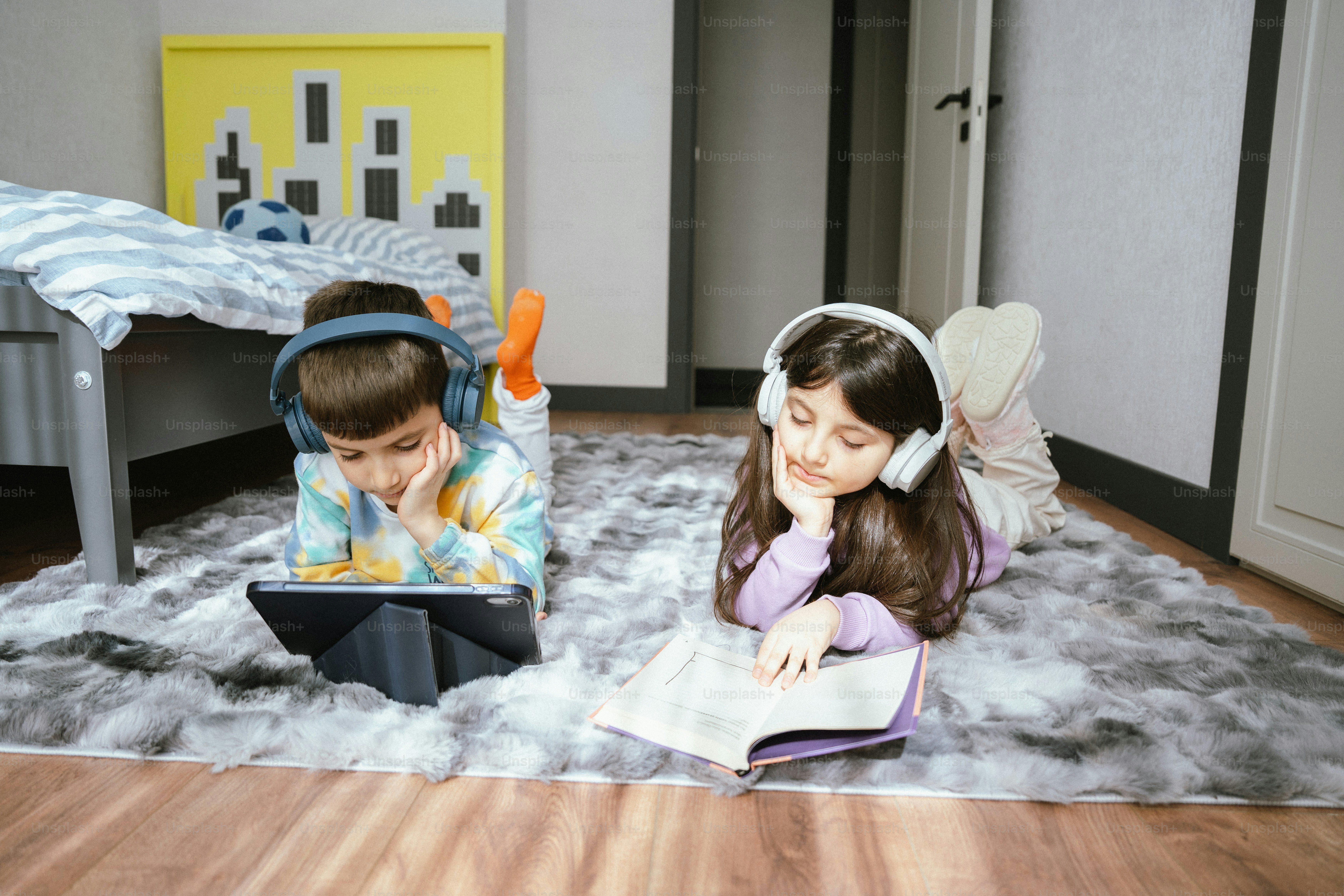 Dos niños con auriculares, uno con tablet, otro leyendo.