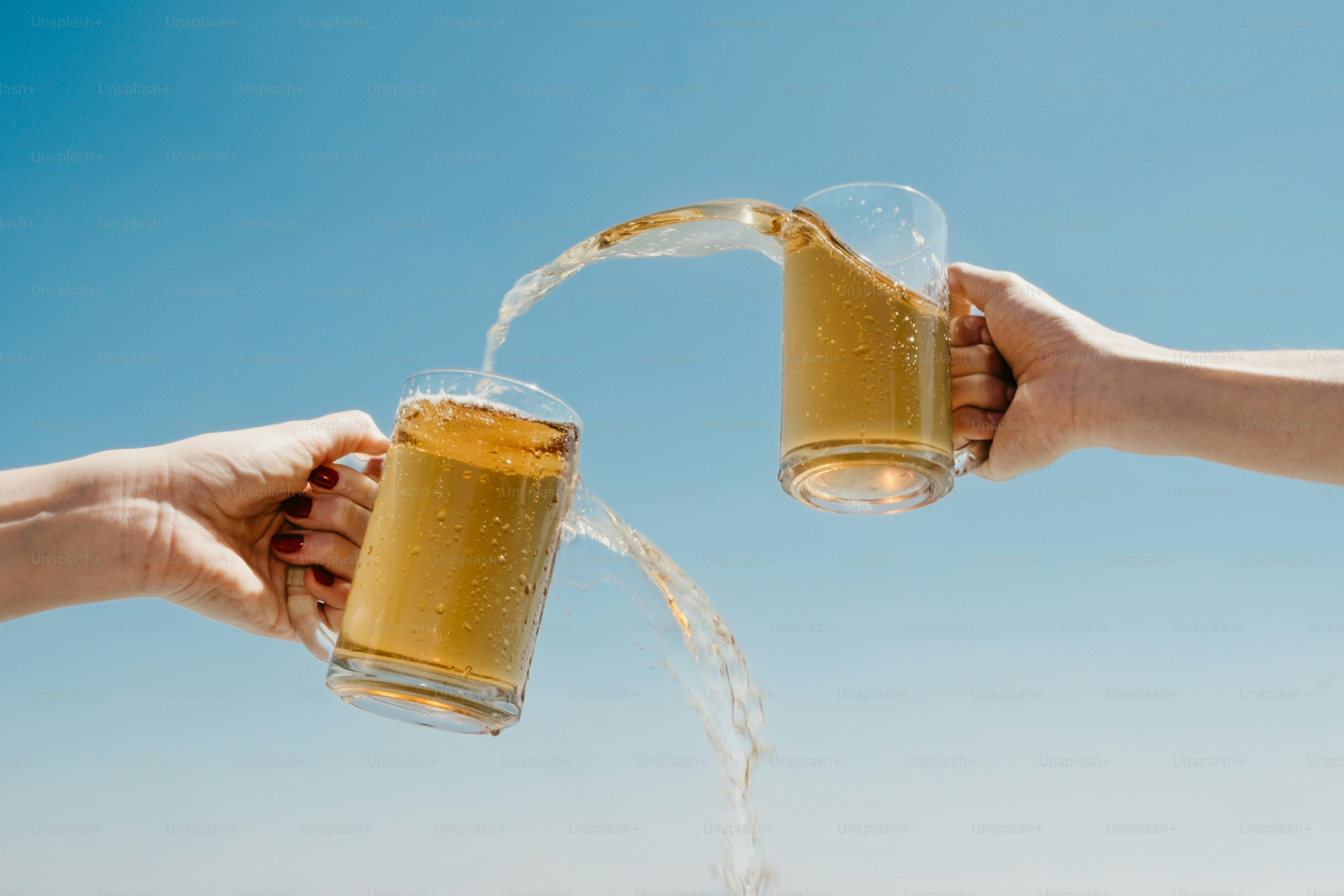 Dos manos chocando jarras de cerveza con líquido salpicando