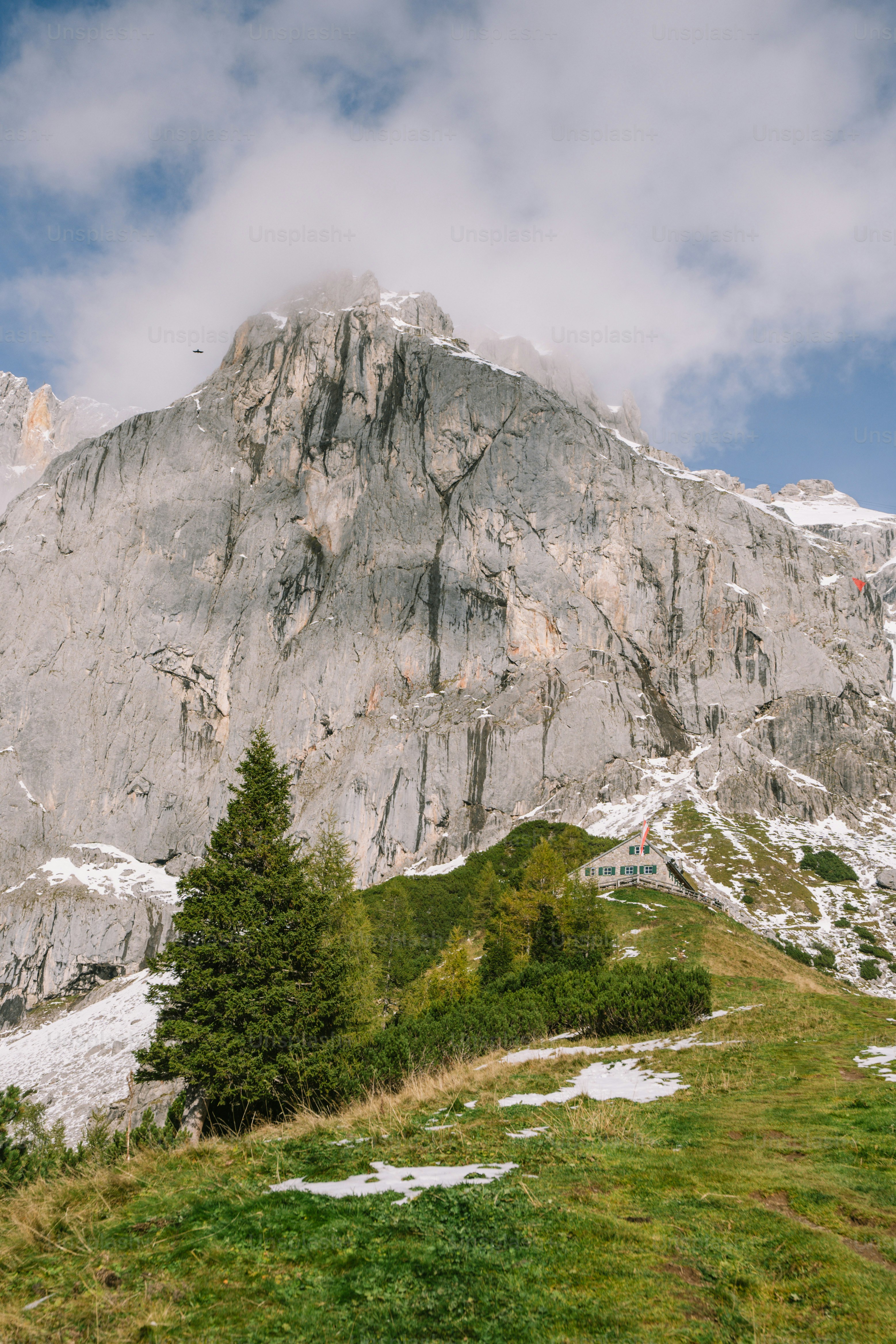 A large rocky mountain with sparse trees and grass. photo – Cloudy sky ...