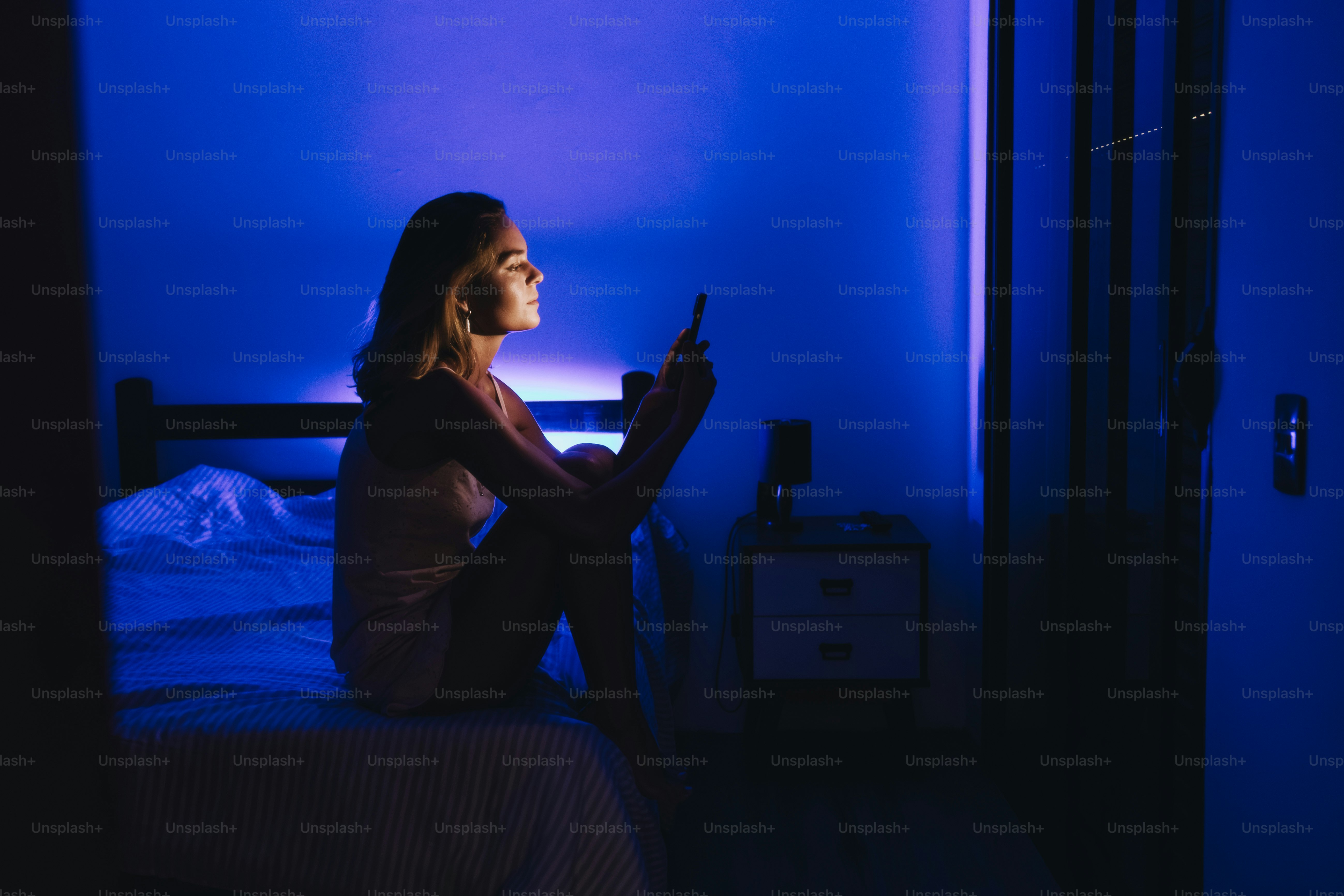 Mujer iluminada por la pantalla del móvil en una habitación oscura