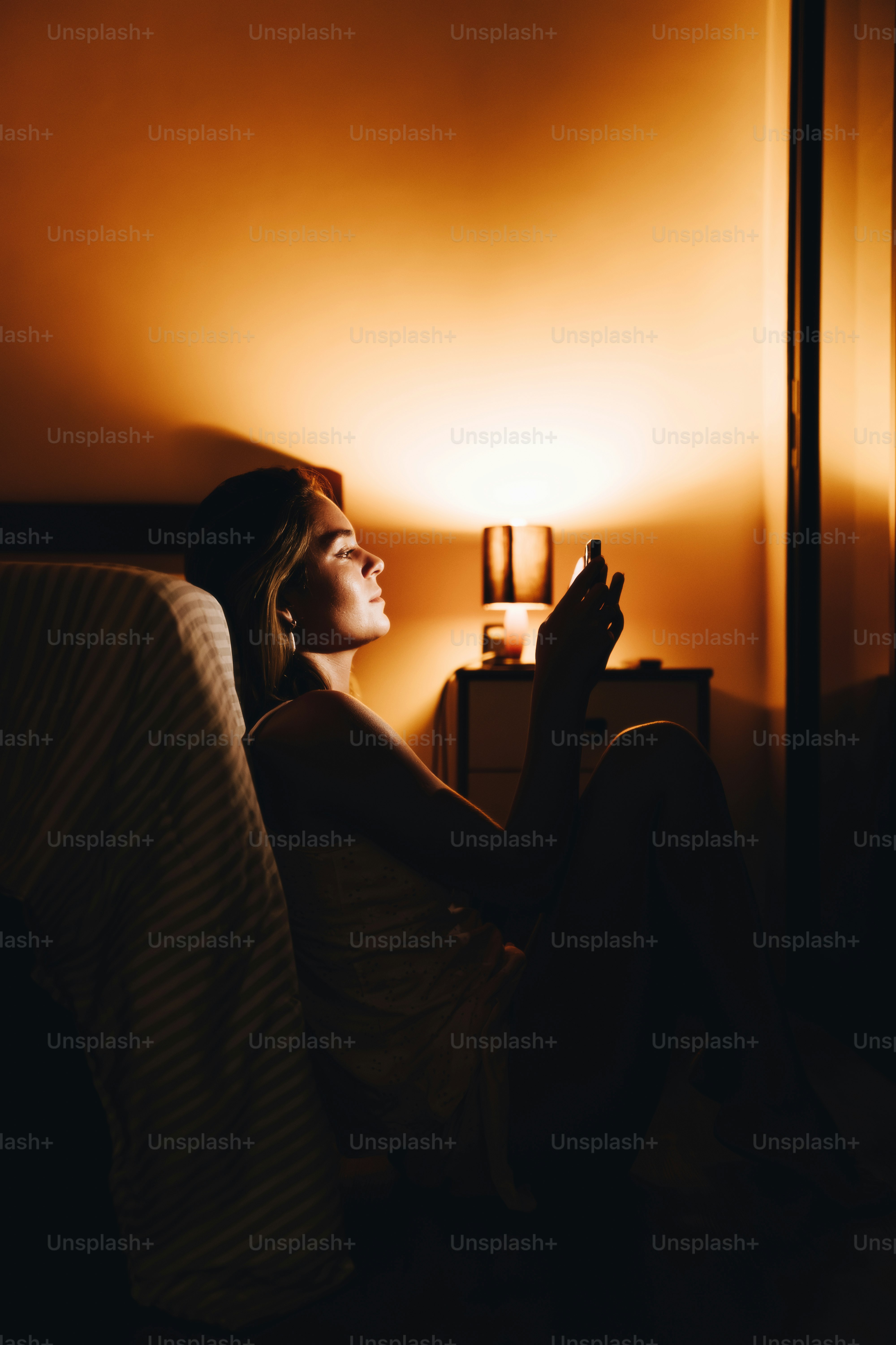 Mujer iluminada por la pantalla del móvil en una habitación oscura.