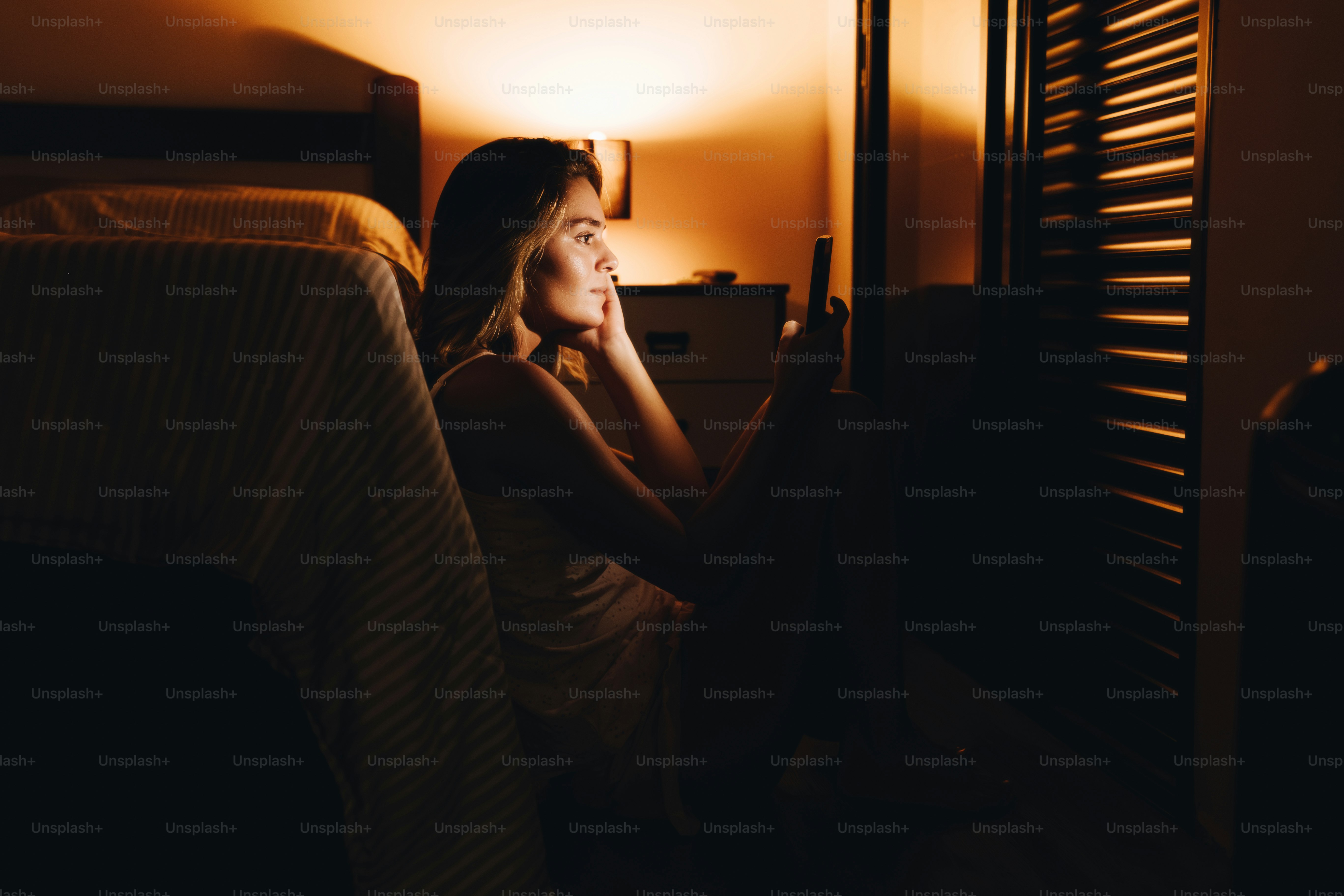 Joven iluminada por la pantalla del móvil por la noche.