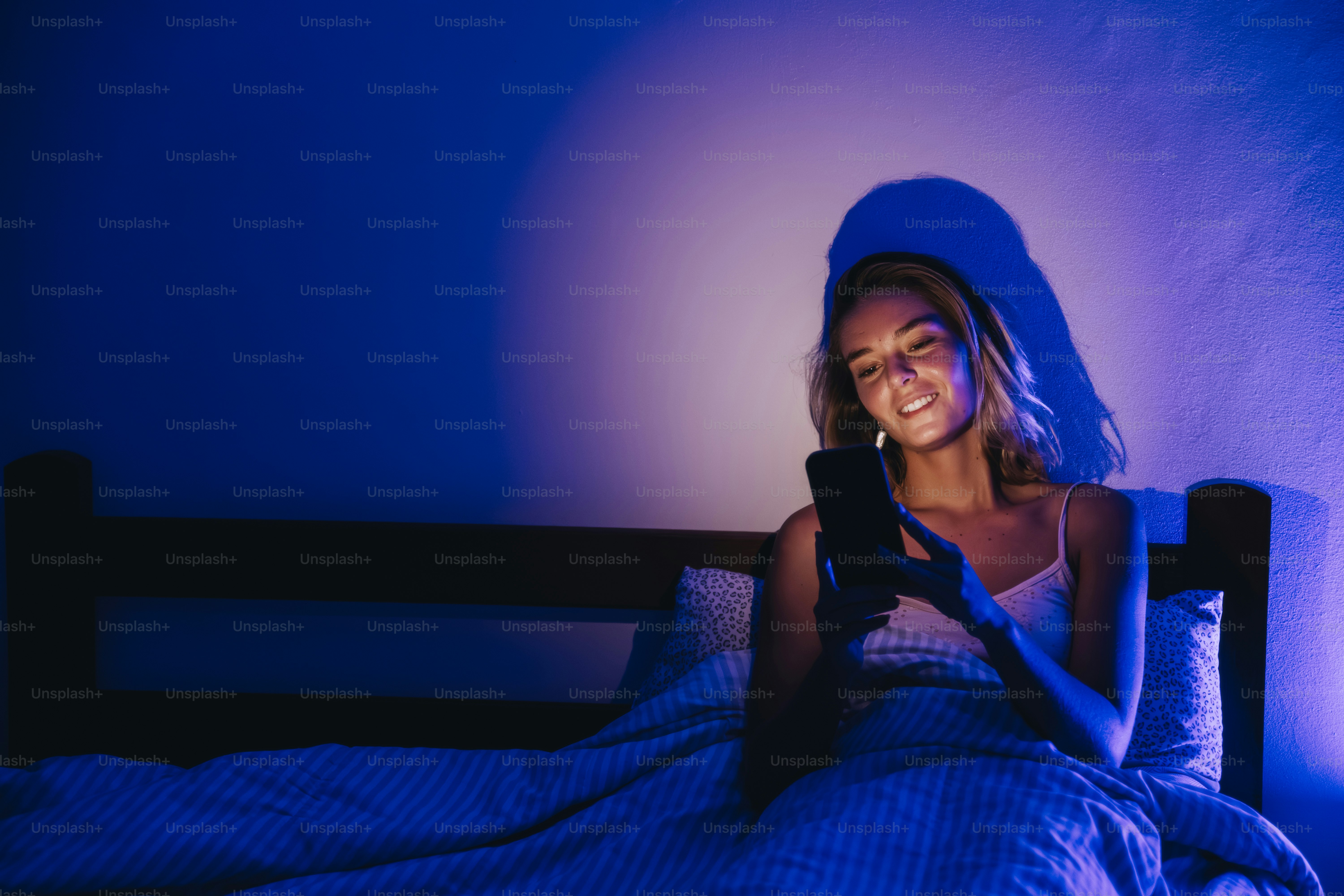 Joven usando el móvil en la cama por la noche.