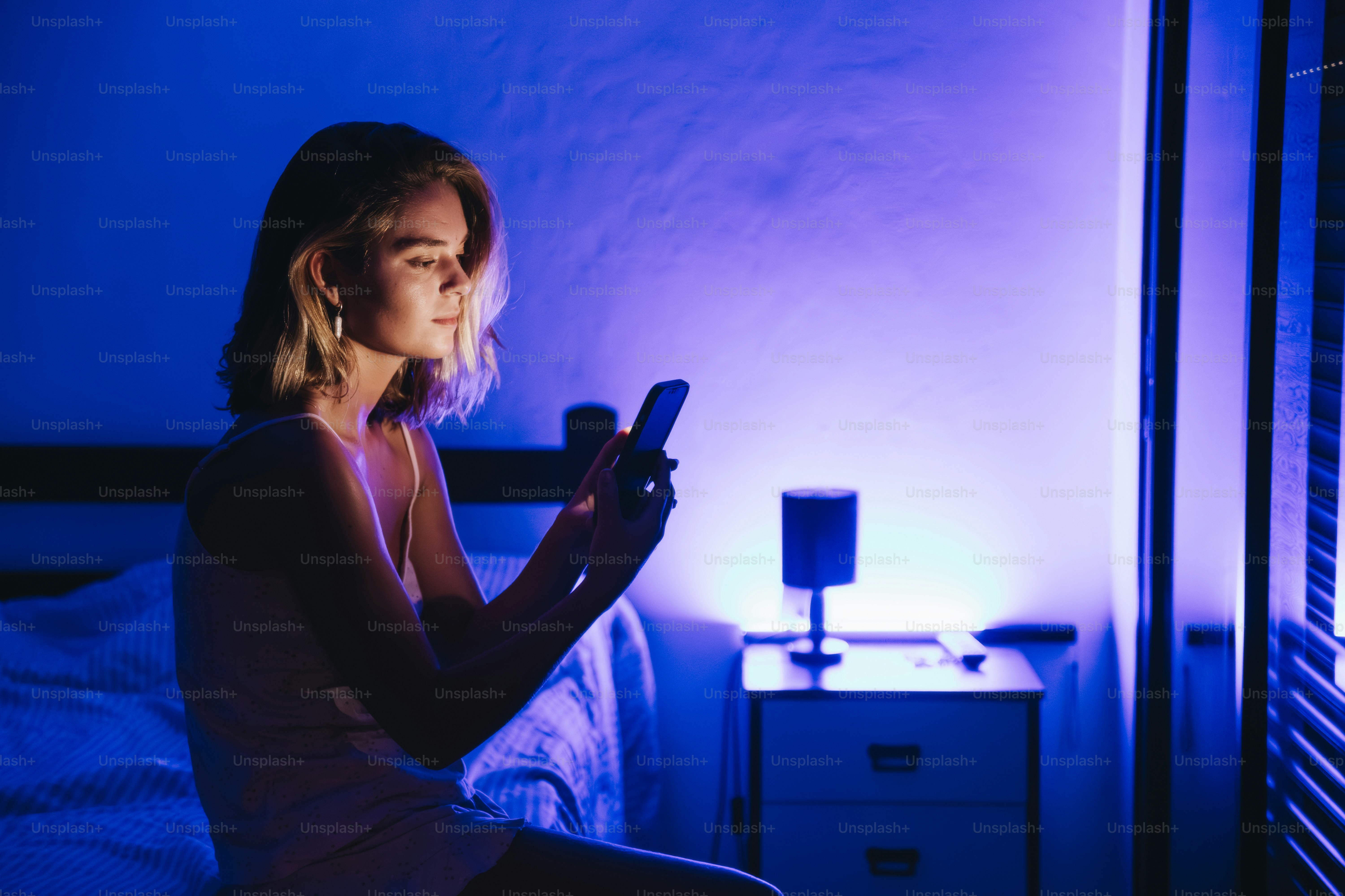 Joven iluminada por la pantalla del móvil en una habitación oscura.