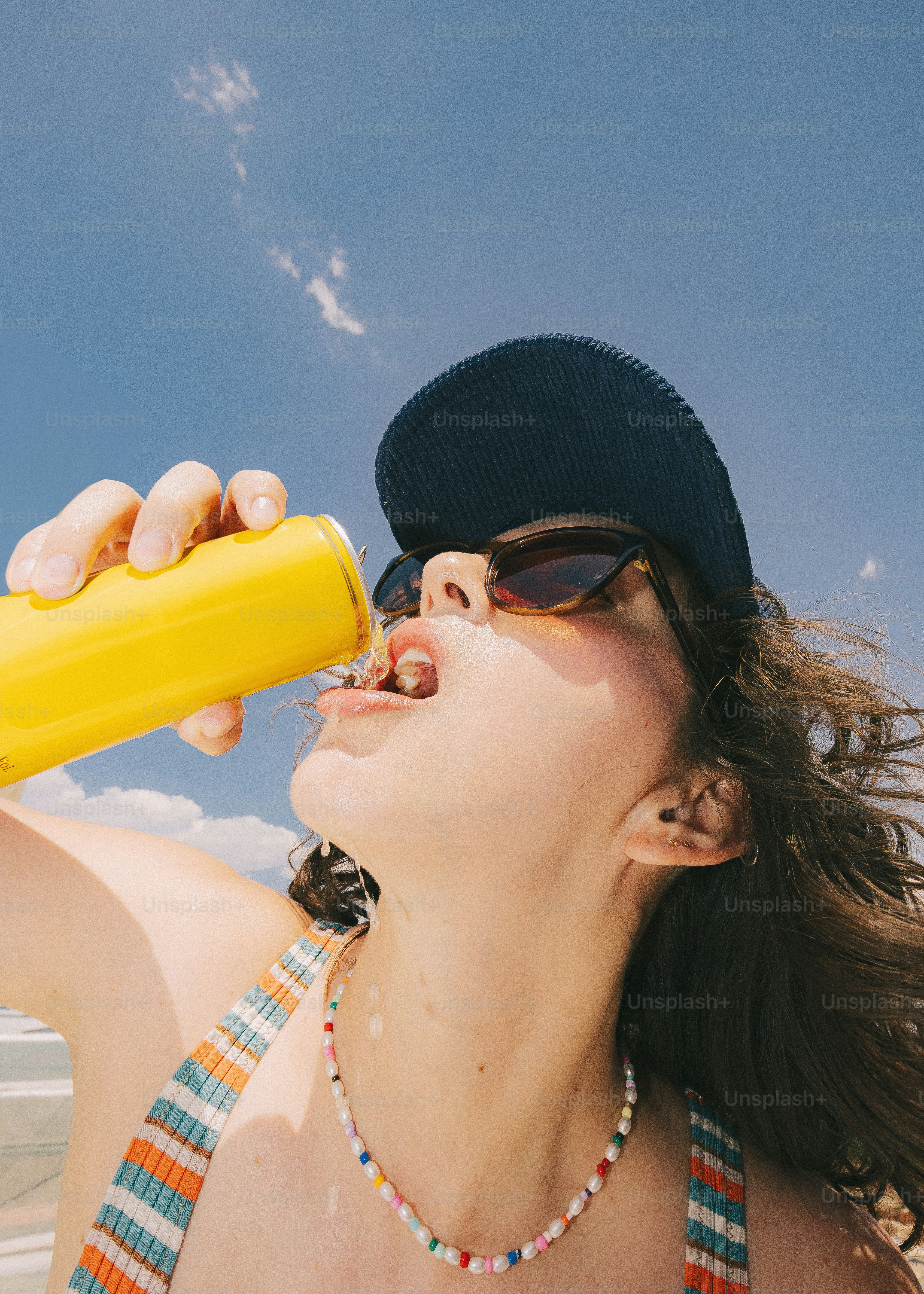 Jeune femme buvant dans une canette jaune sous un ciel bleu
