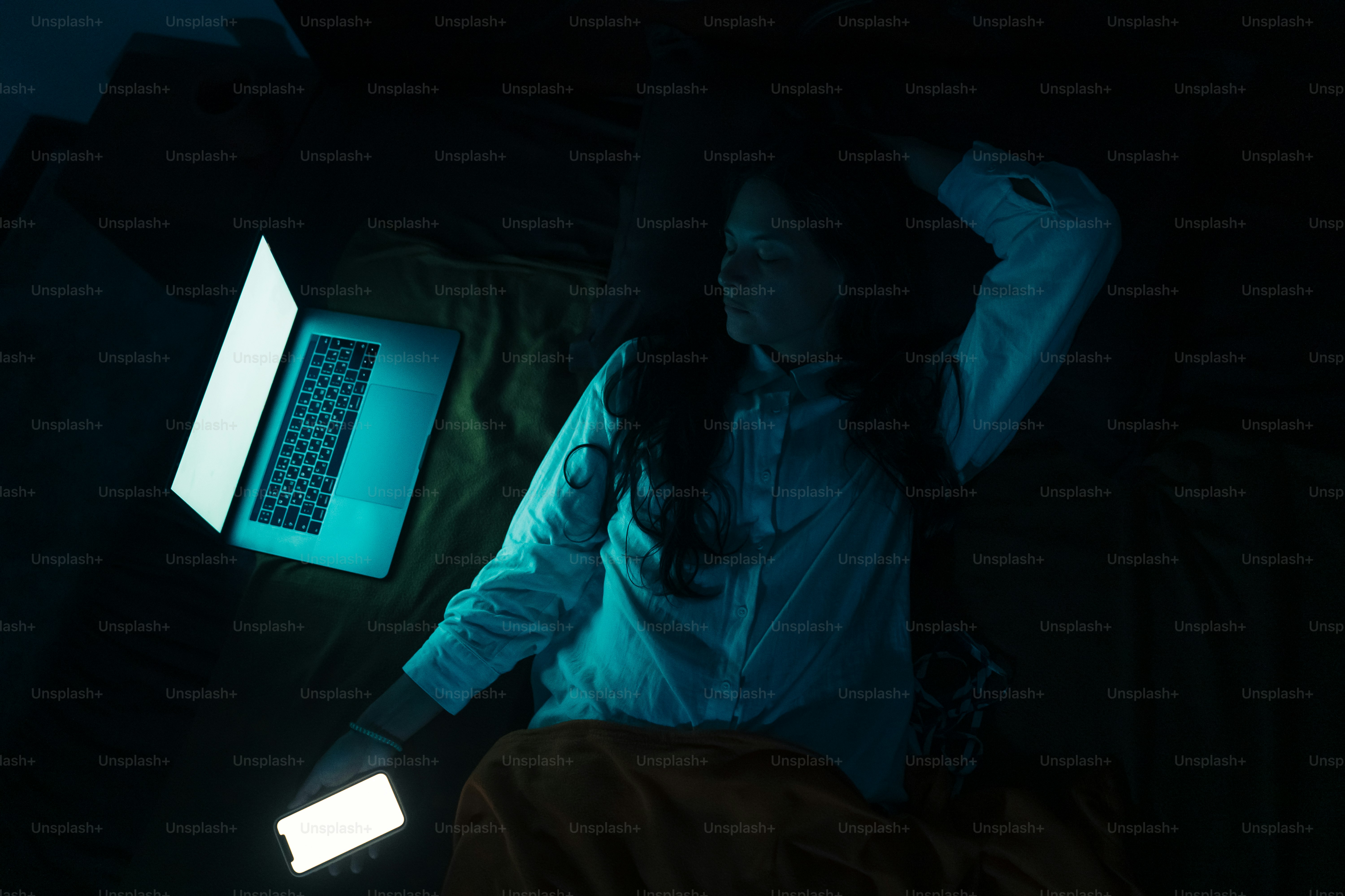 Wanita di tempat tidur dengan laptop dan telepon di malam hari
