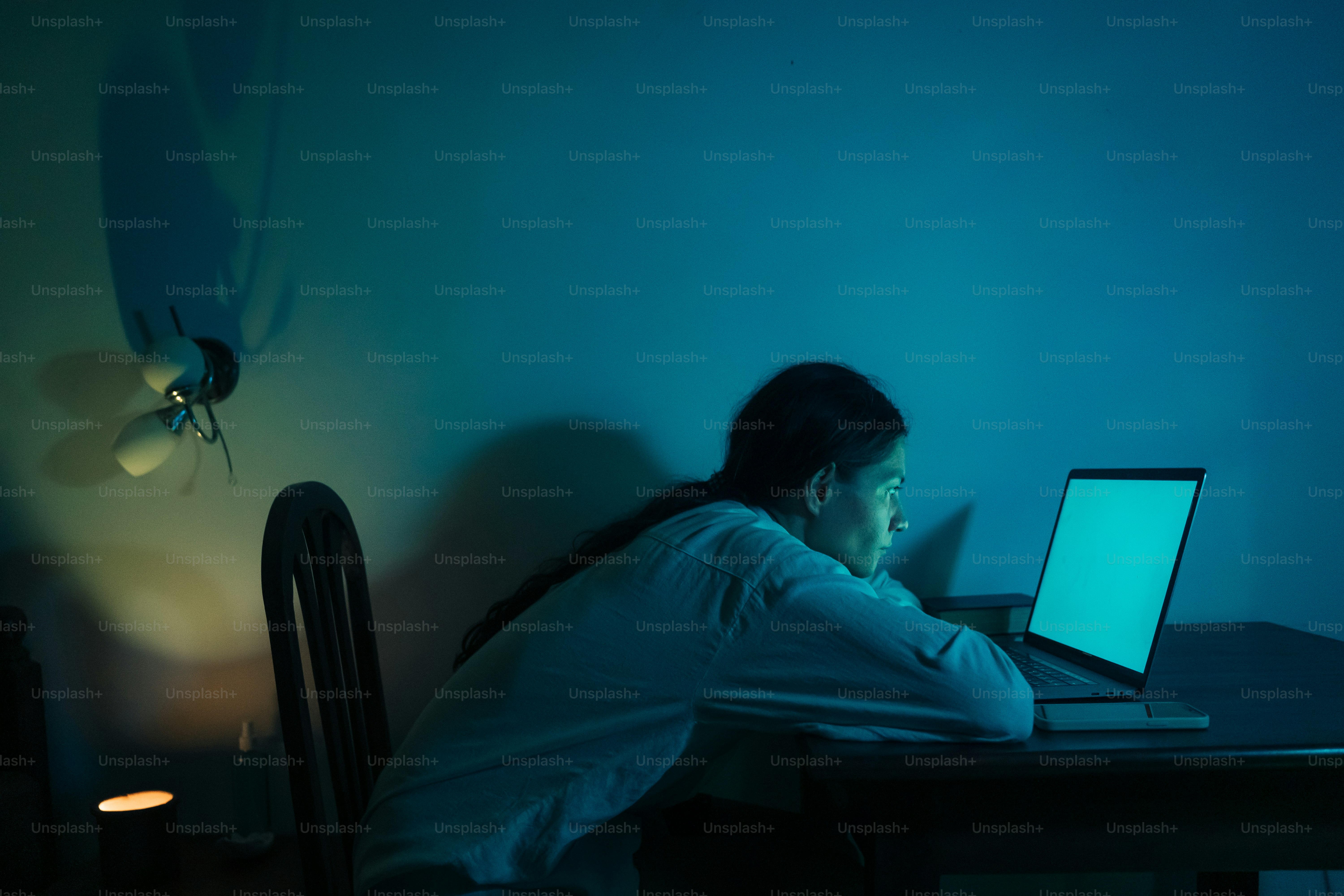 Wanita muda yang bekerja di laptop di ruangan yang remang-remang