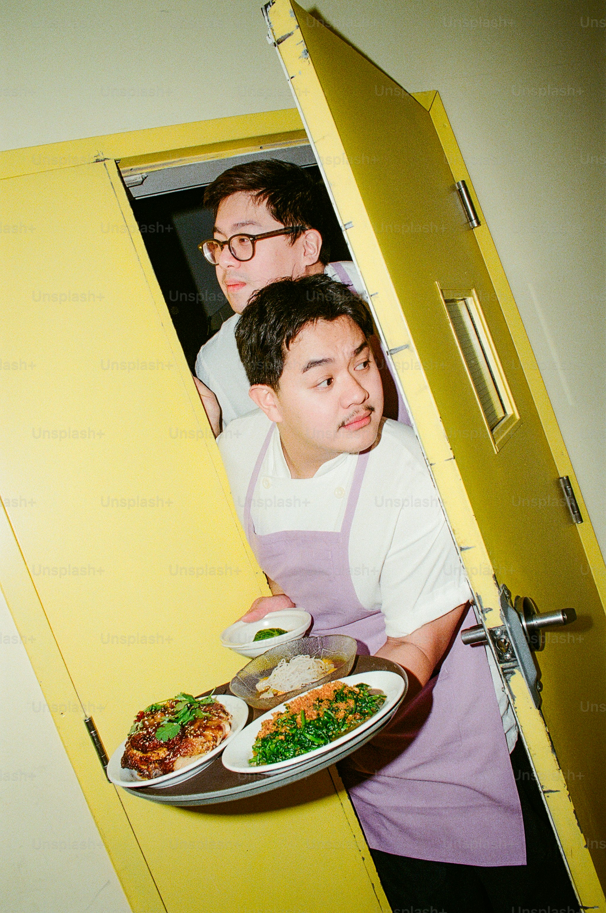 黄色いドアの向こうから食べ物を運ぶ二人の男