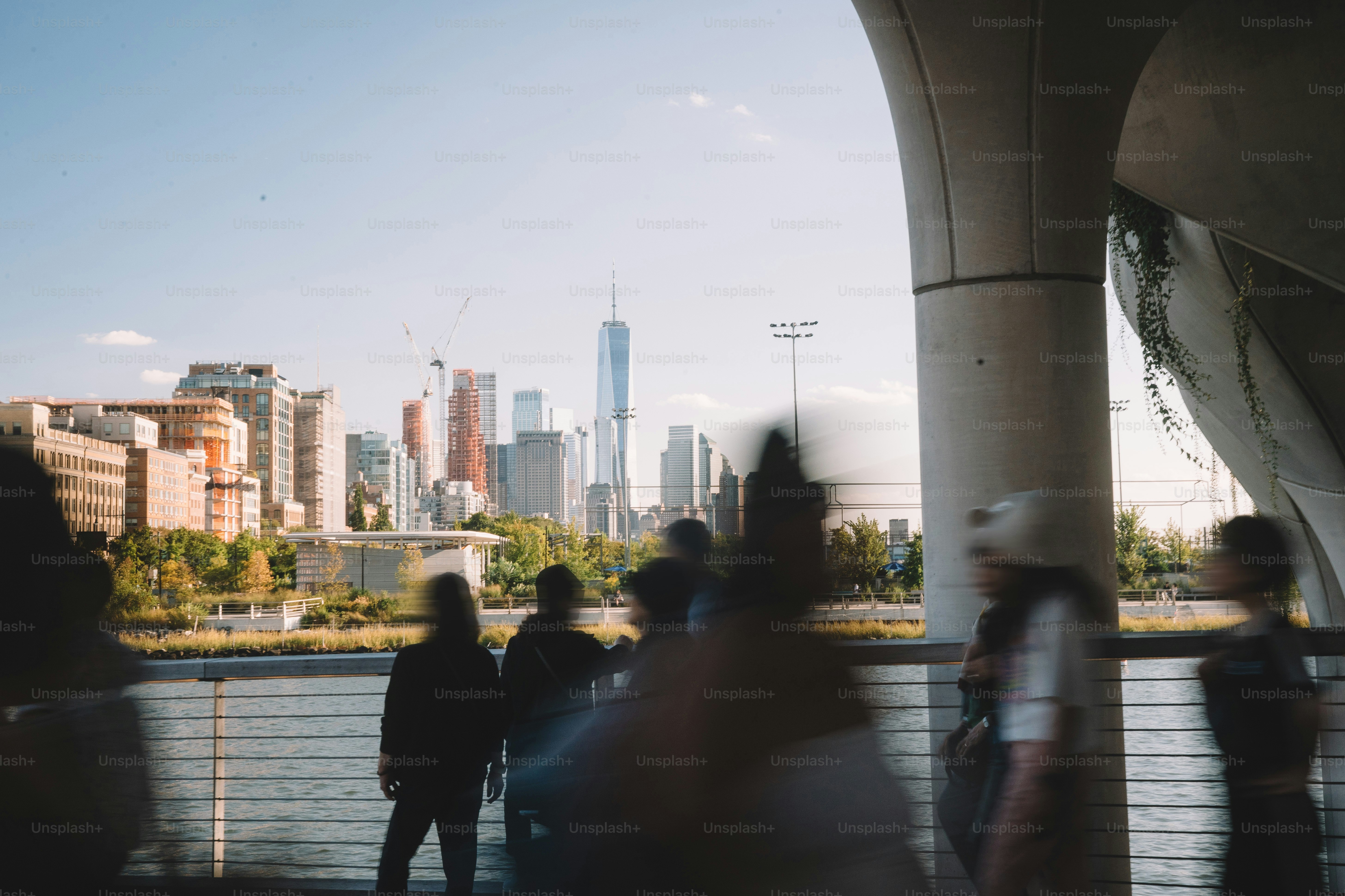 People walk along a waterfront with city skyline.