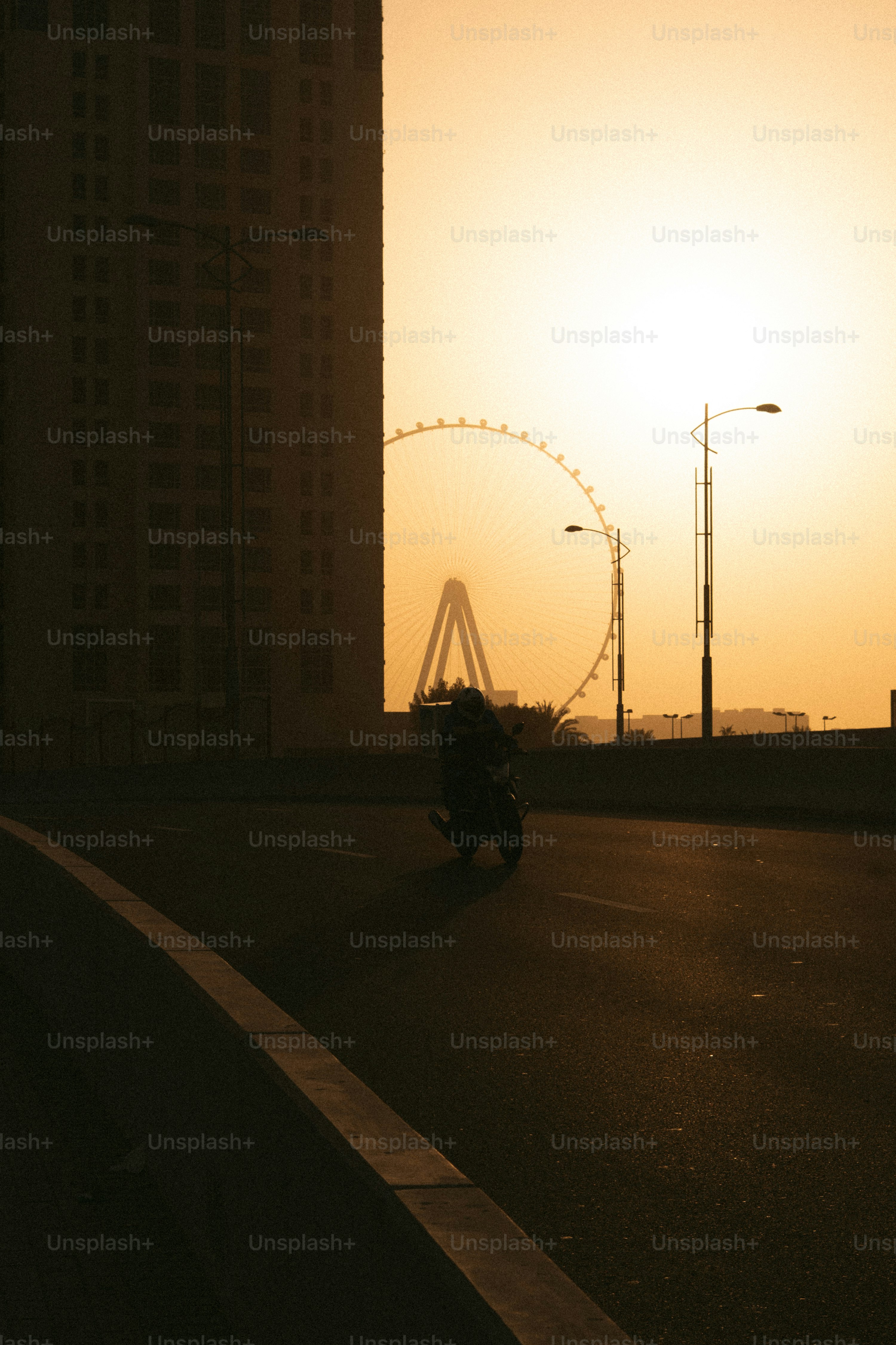 Motorradfahrer fährt bei Sonnenuntergang an einem Riesenrad vorbei