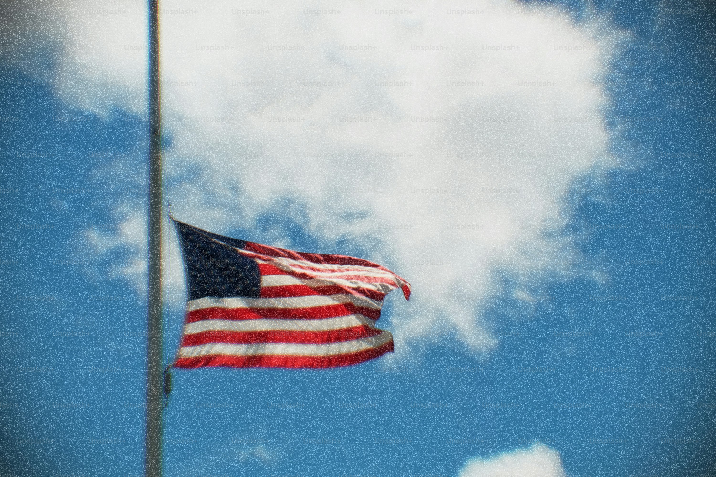 American flag waving against a cloudy blue sky.