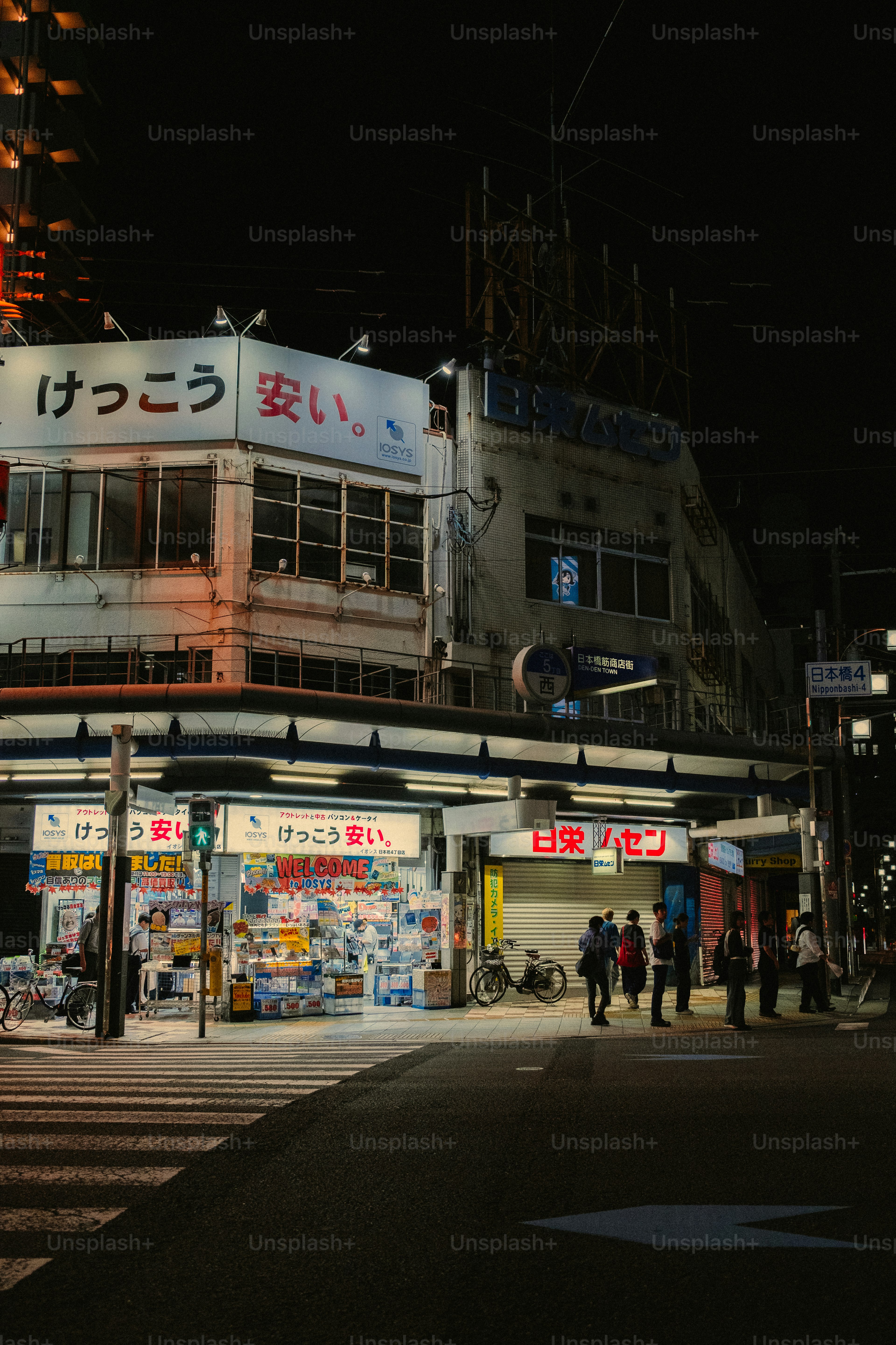 Street scene at night with illuminated buildings and people.