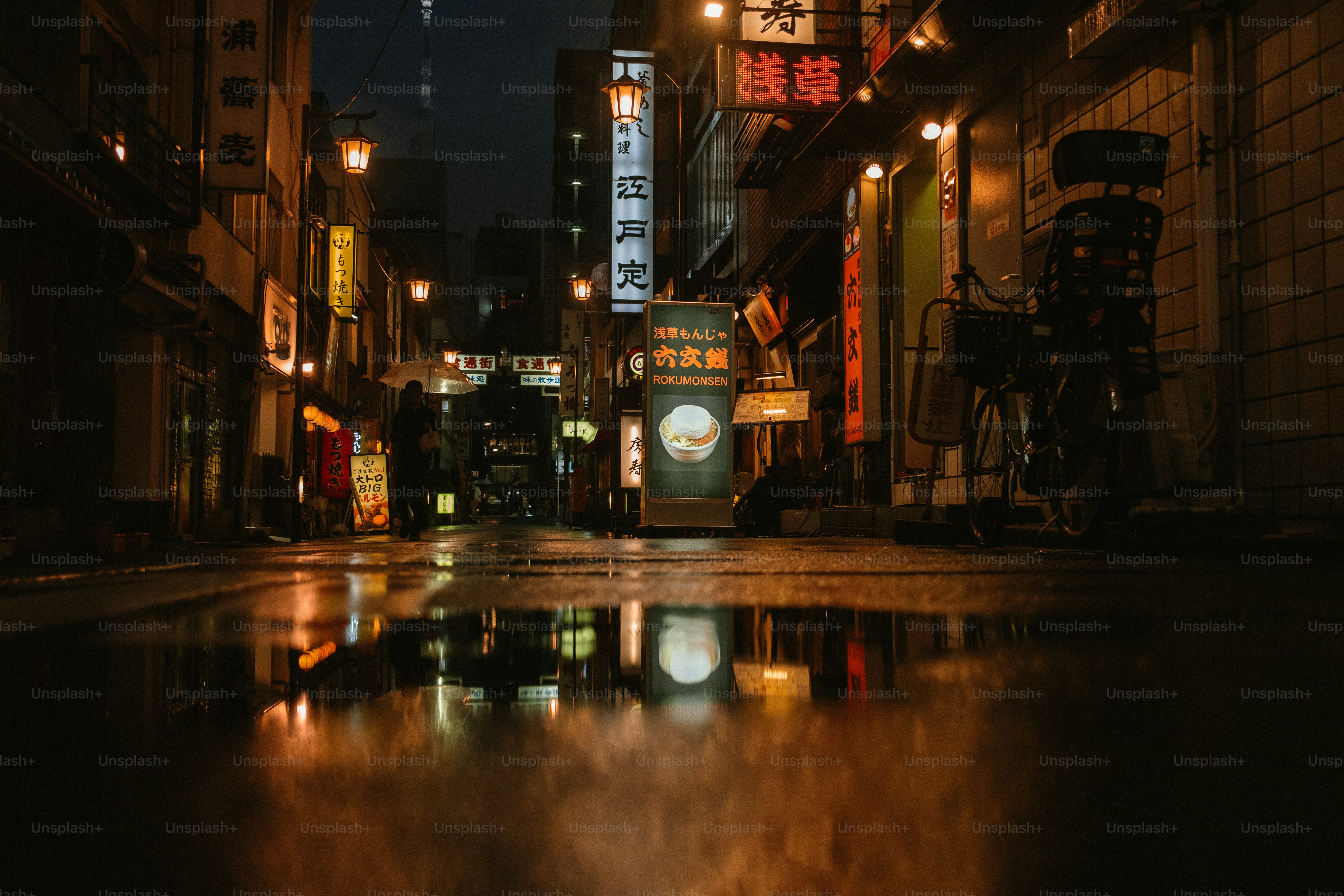 Jalan basah yang memantulkan lampu di kota Jepang di malam hari.