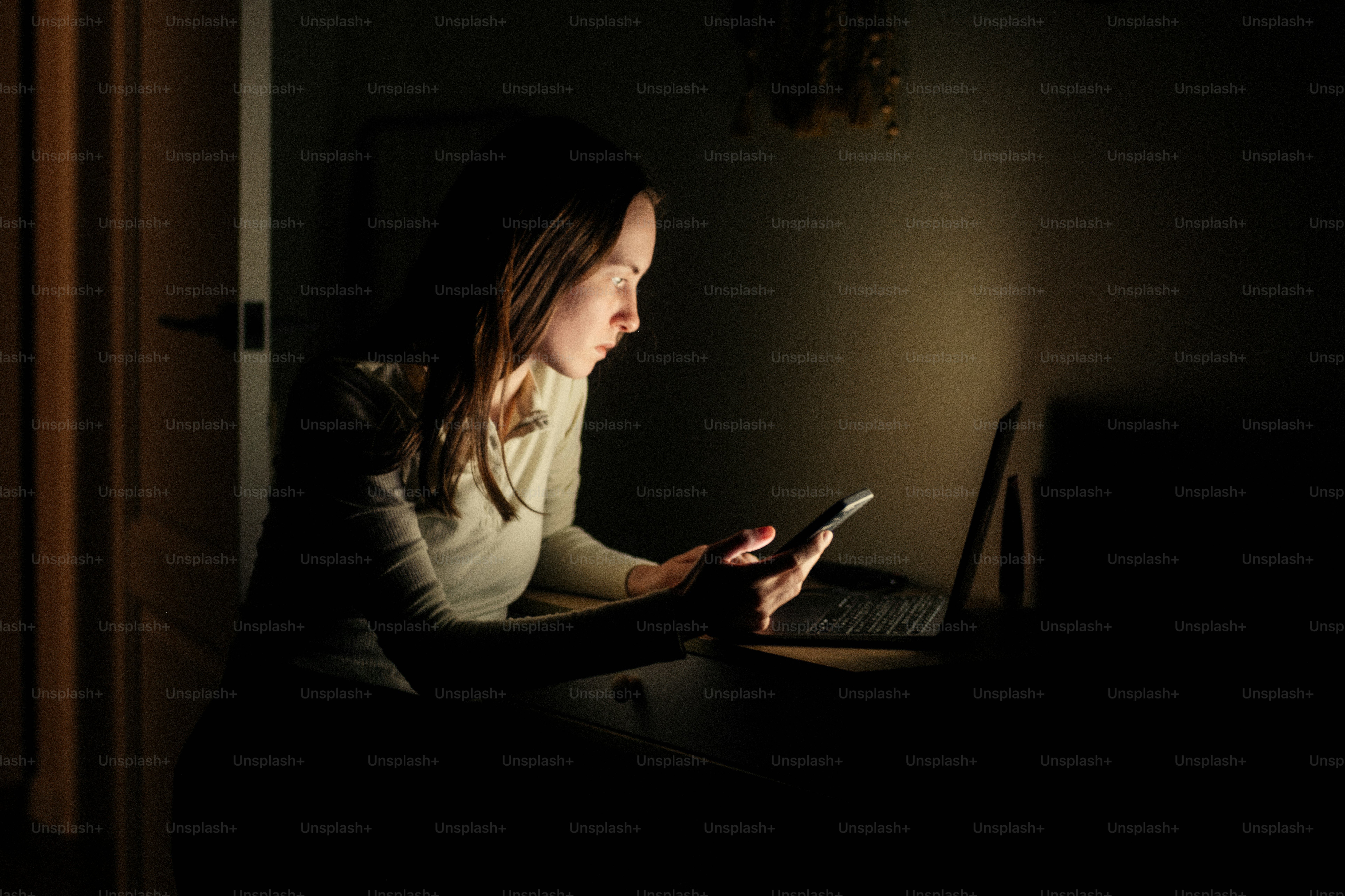 Frau benutzt Handy und Laptop im Dunkelraum