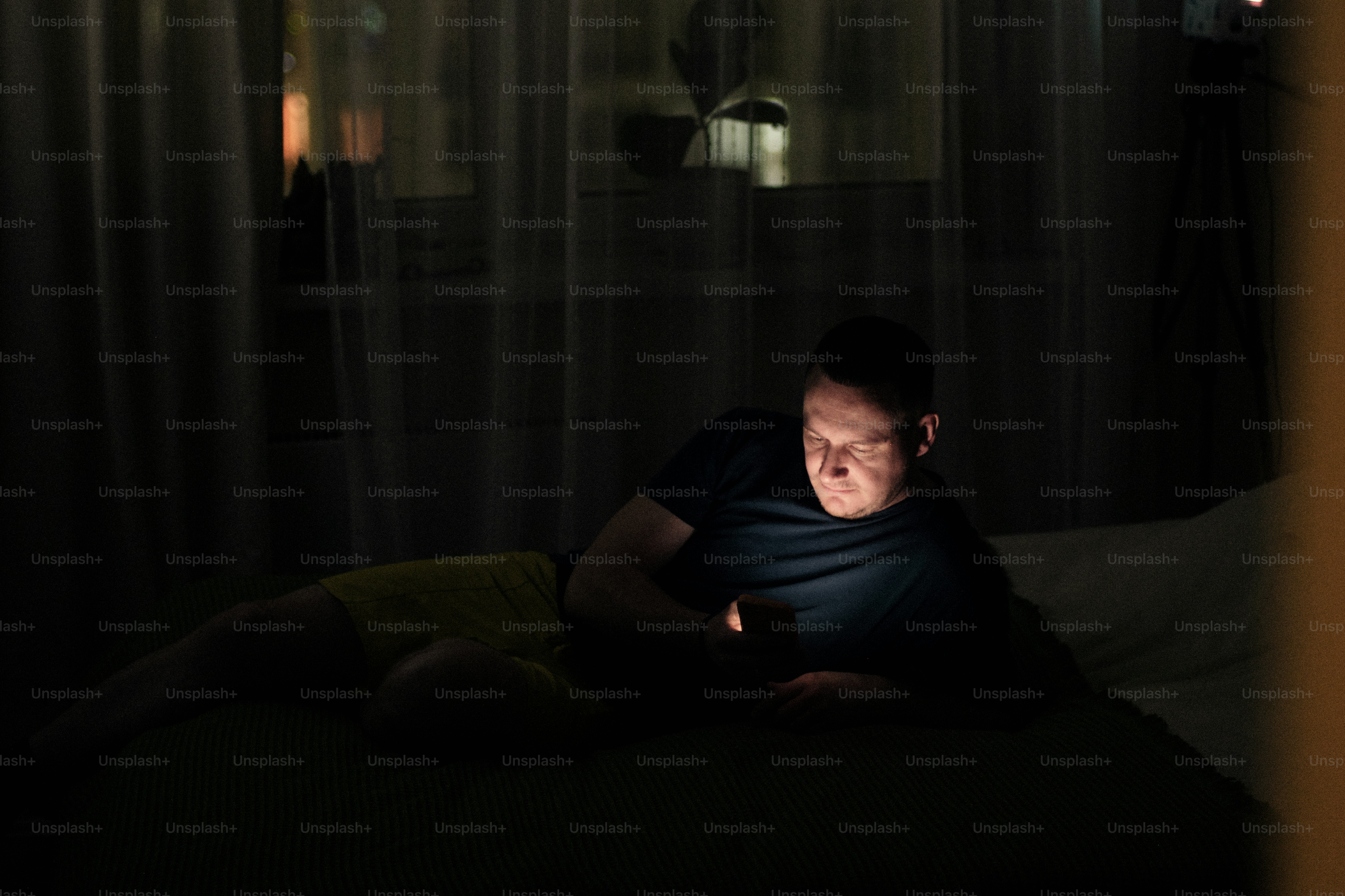 Mann liegt nachts im Bett und schaut aufs Handy.