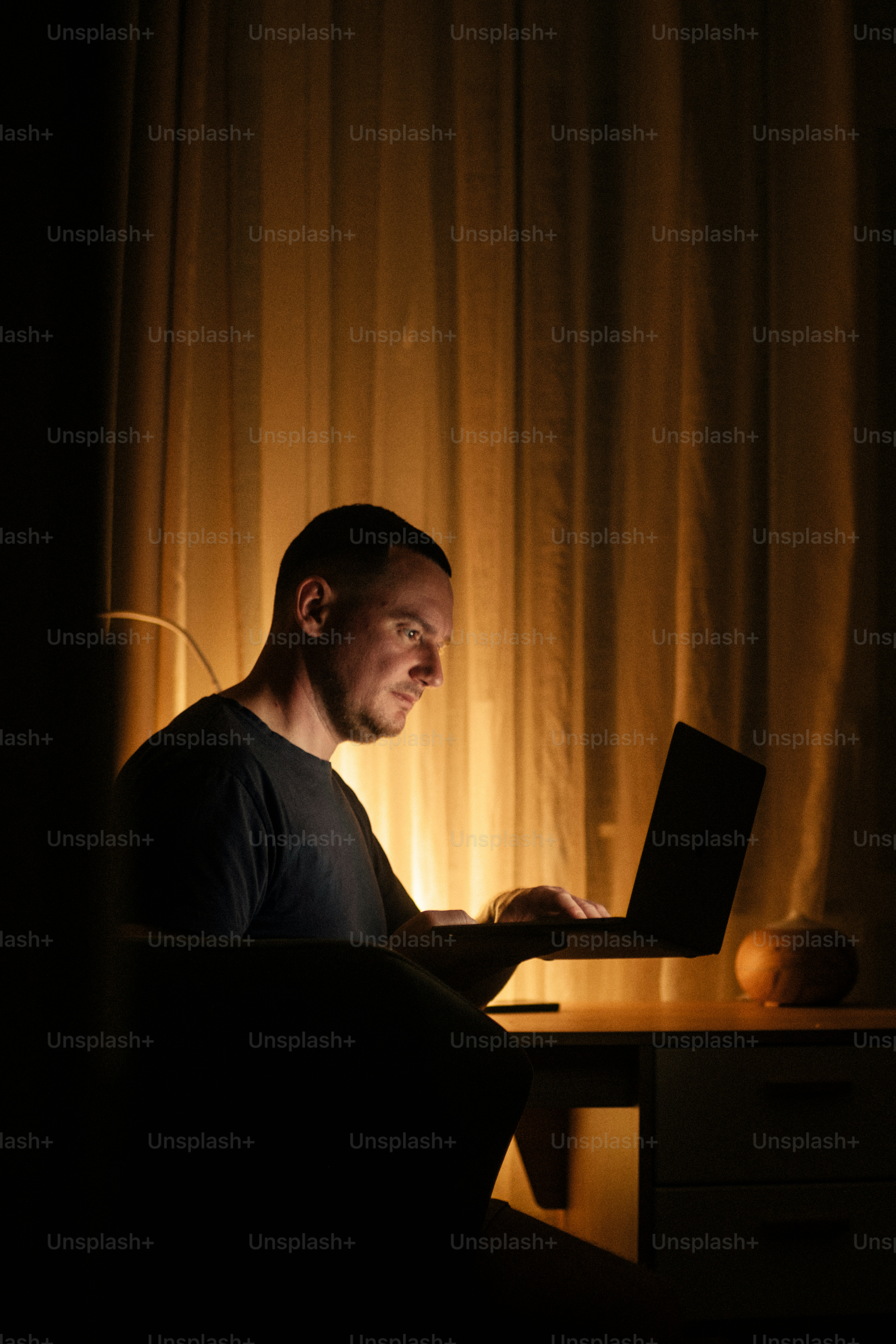 Mann arbeitet am Laptop in einem schwach beleuchteten Raum.