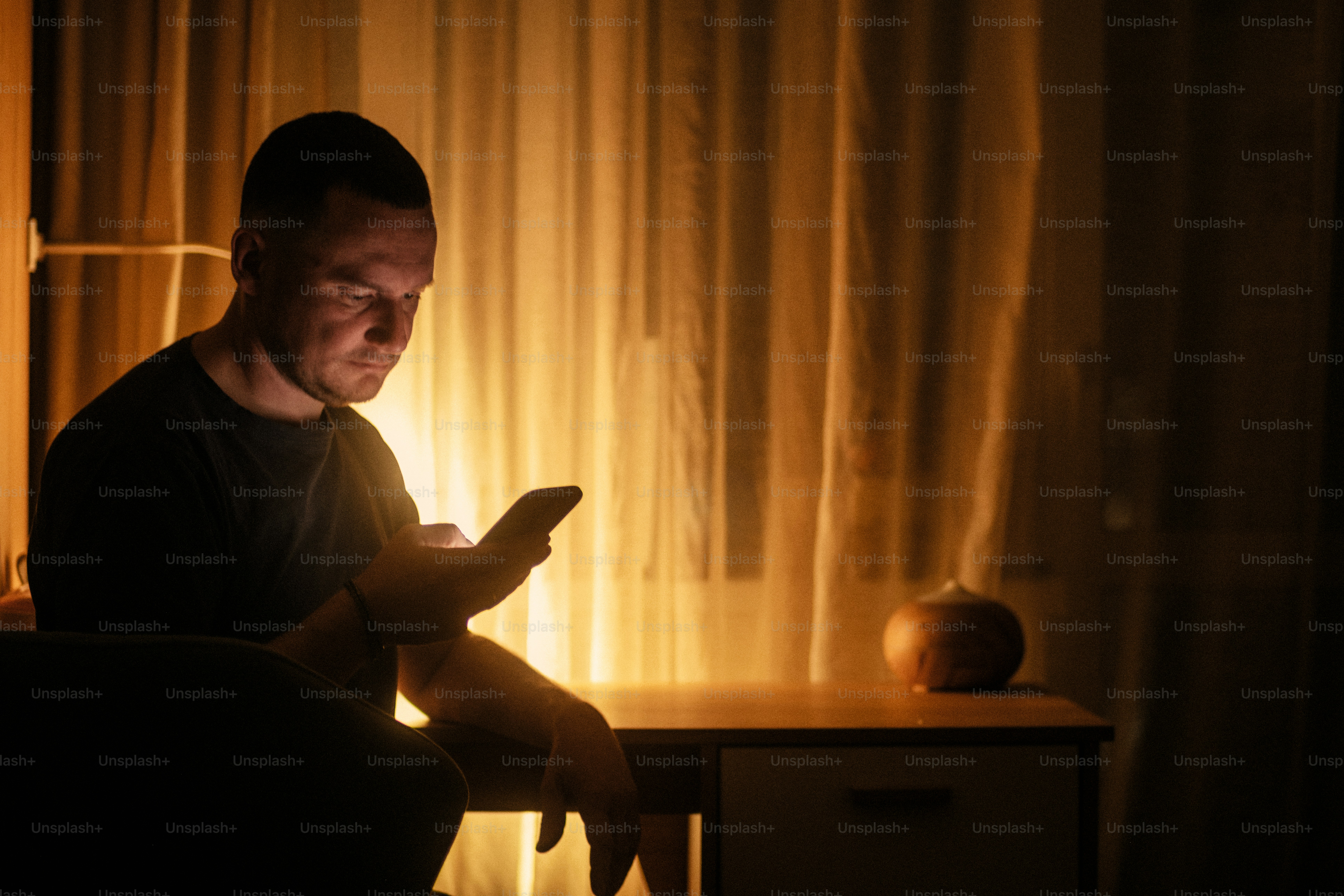 Mann schaut im schwach beleuchteten Raum aufs Handy