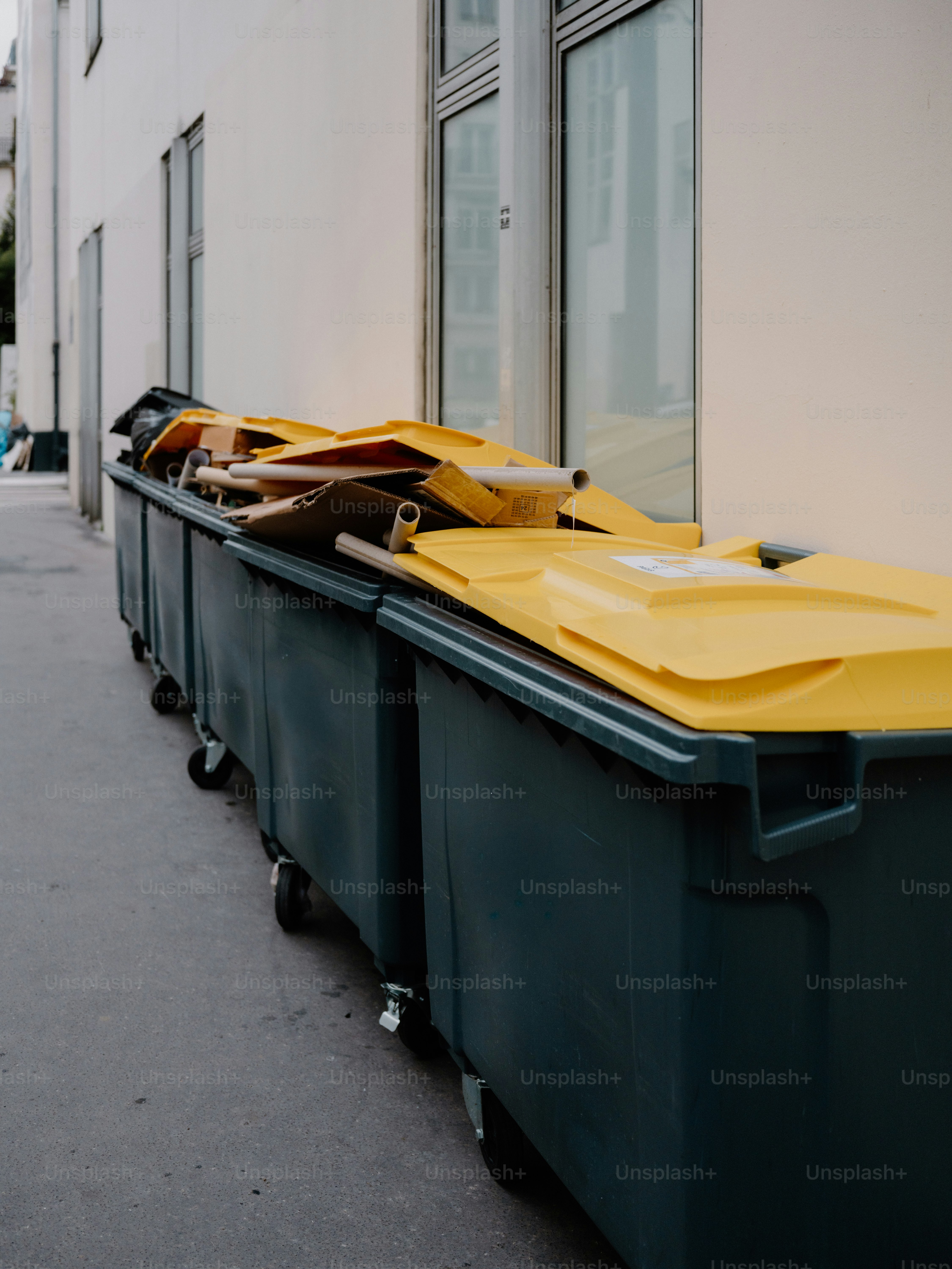 Deretan tempat sampah hijau tua besar dengan tutup kuning