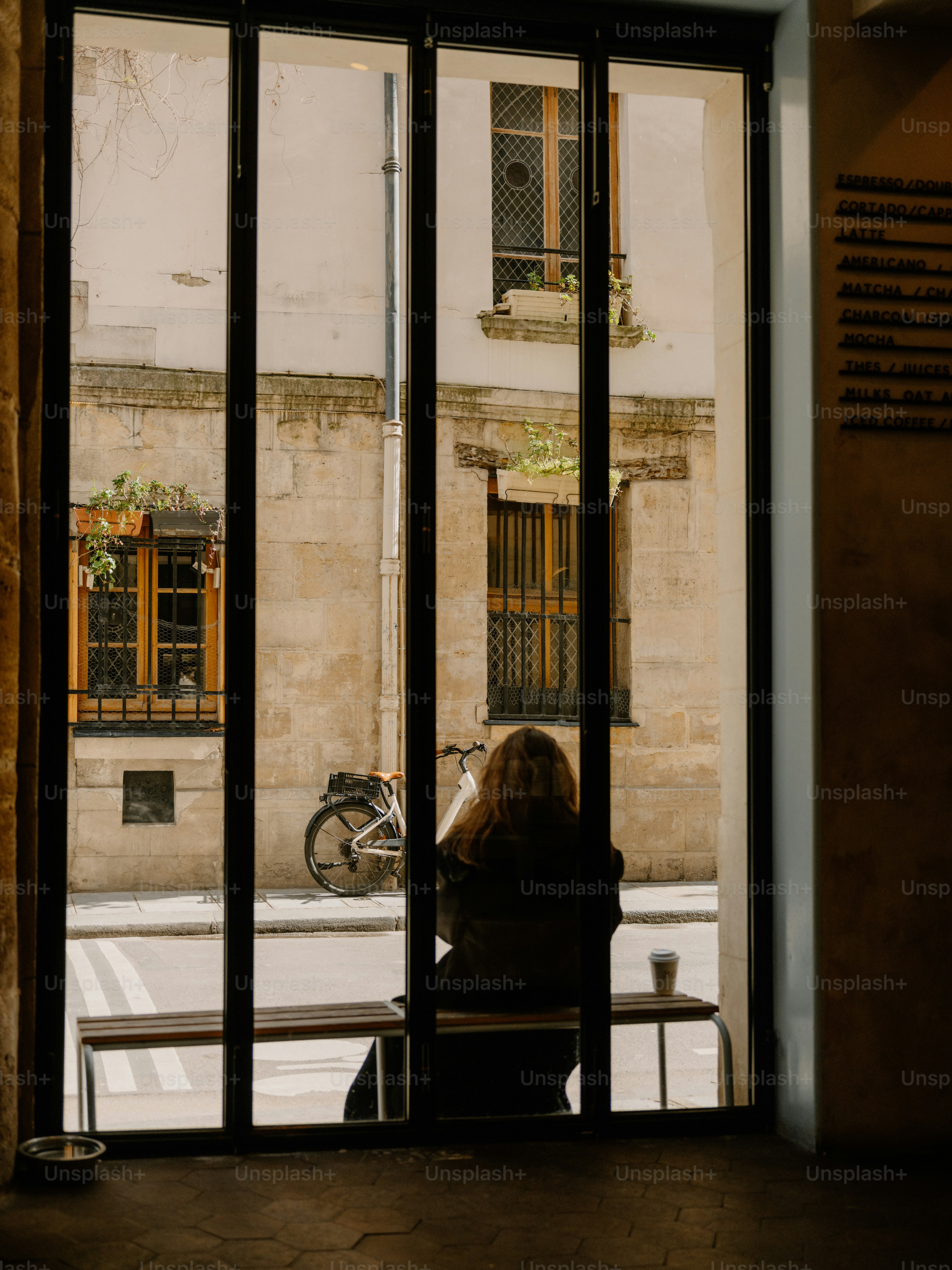 Woman sitting on bench outside cafe looking at street