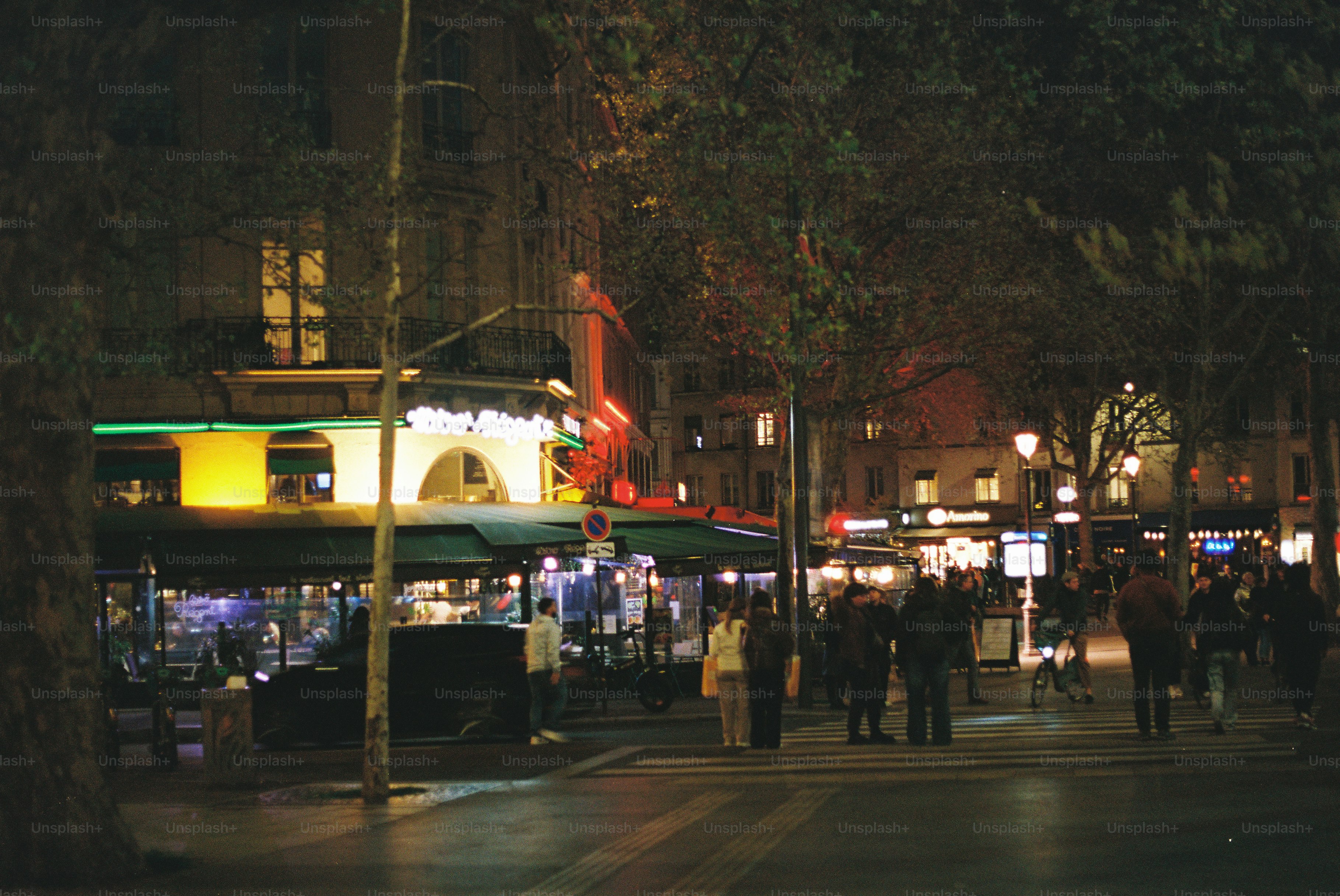 People walking on a street at night with illuminated buildings.