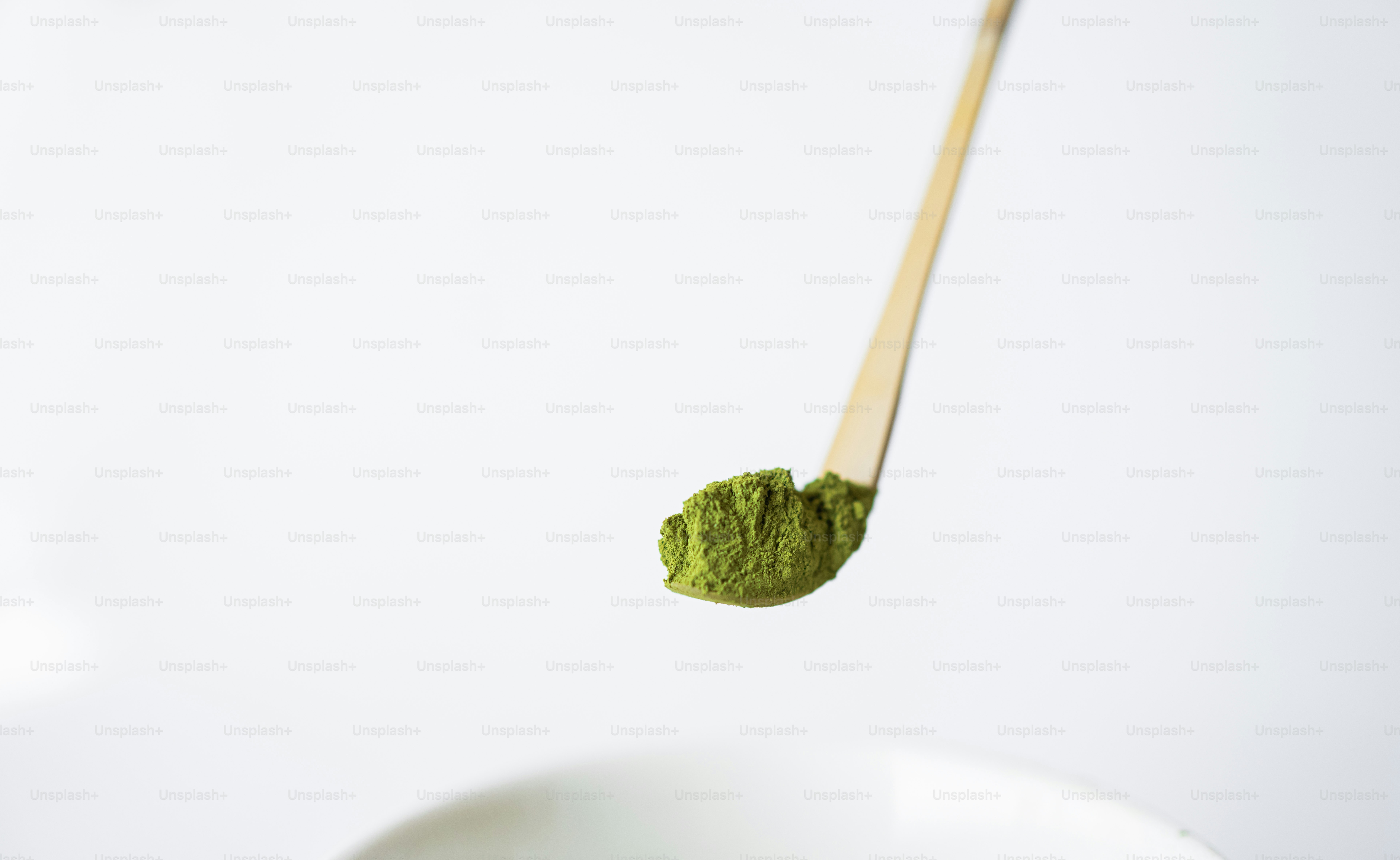 A wooden spoon scoops bright green matcha powder.