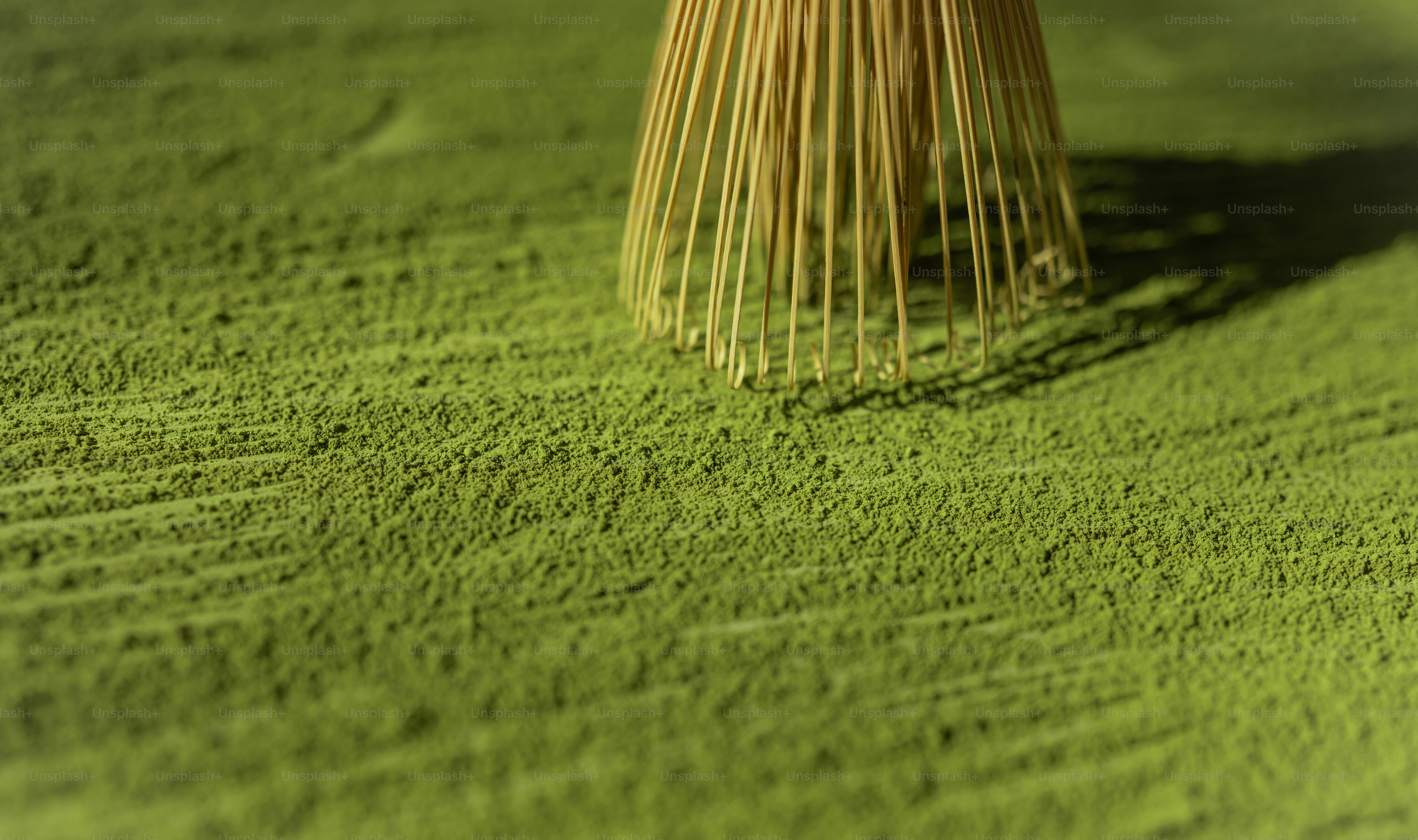 A bamboo whisk rests on a pile of matcha powder.