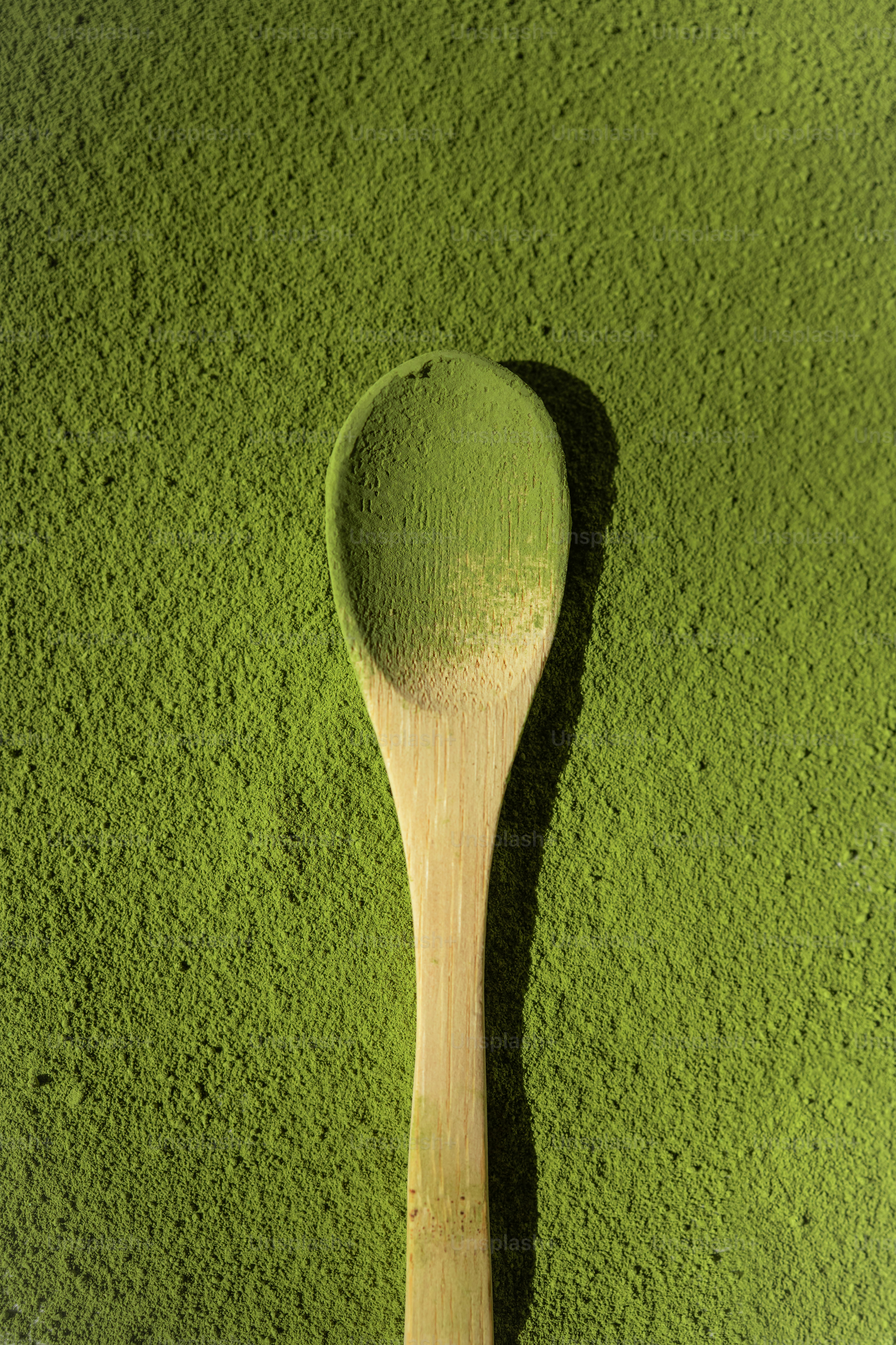A wooden spoon rests on a pile of green powder.