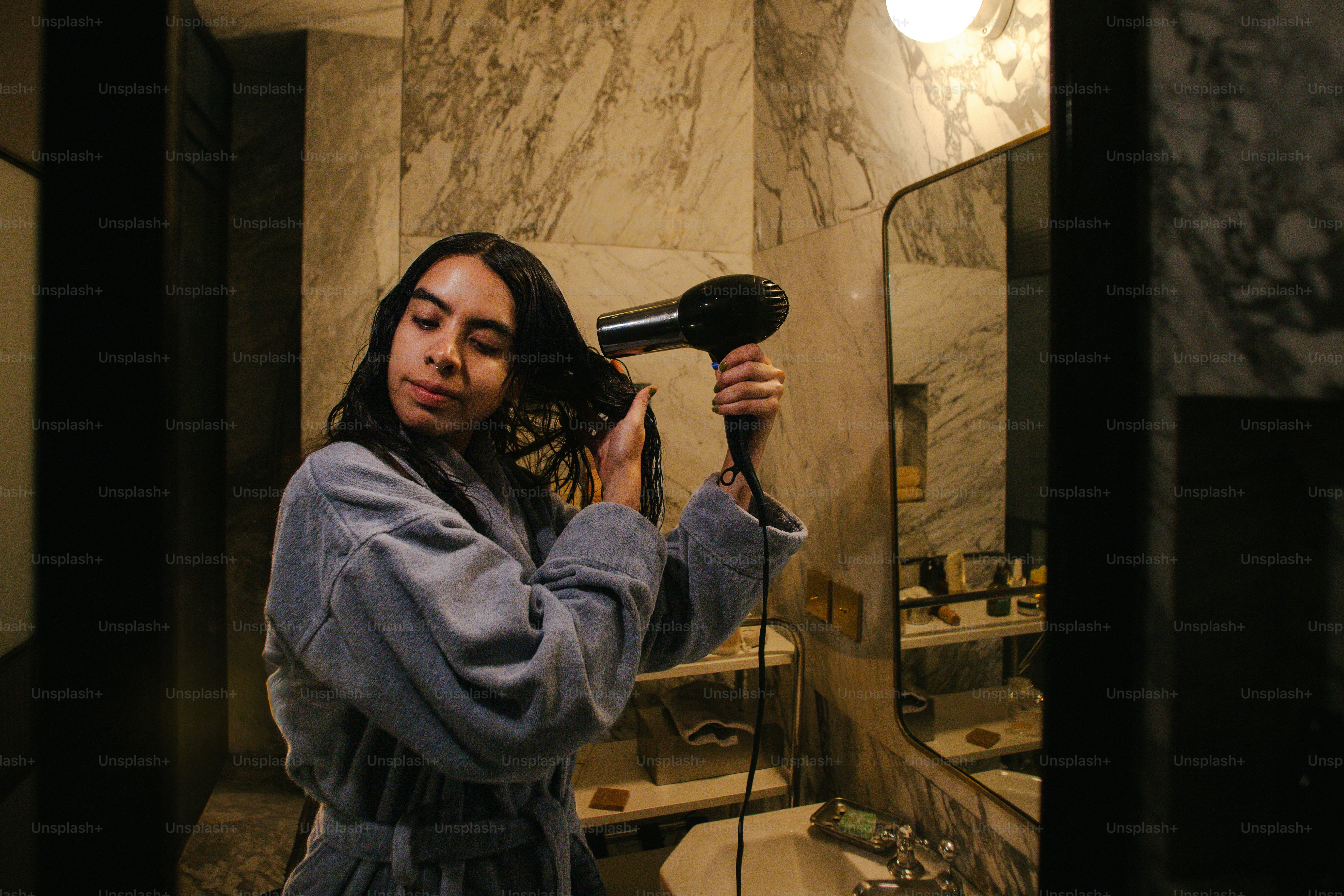 Donna che si asciuga i capelli con un phon in bagno.