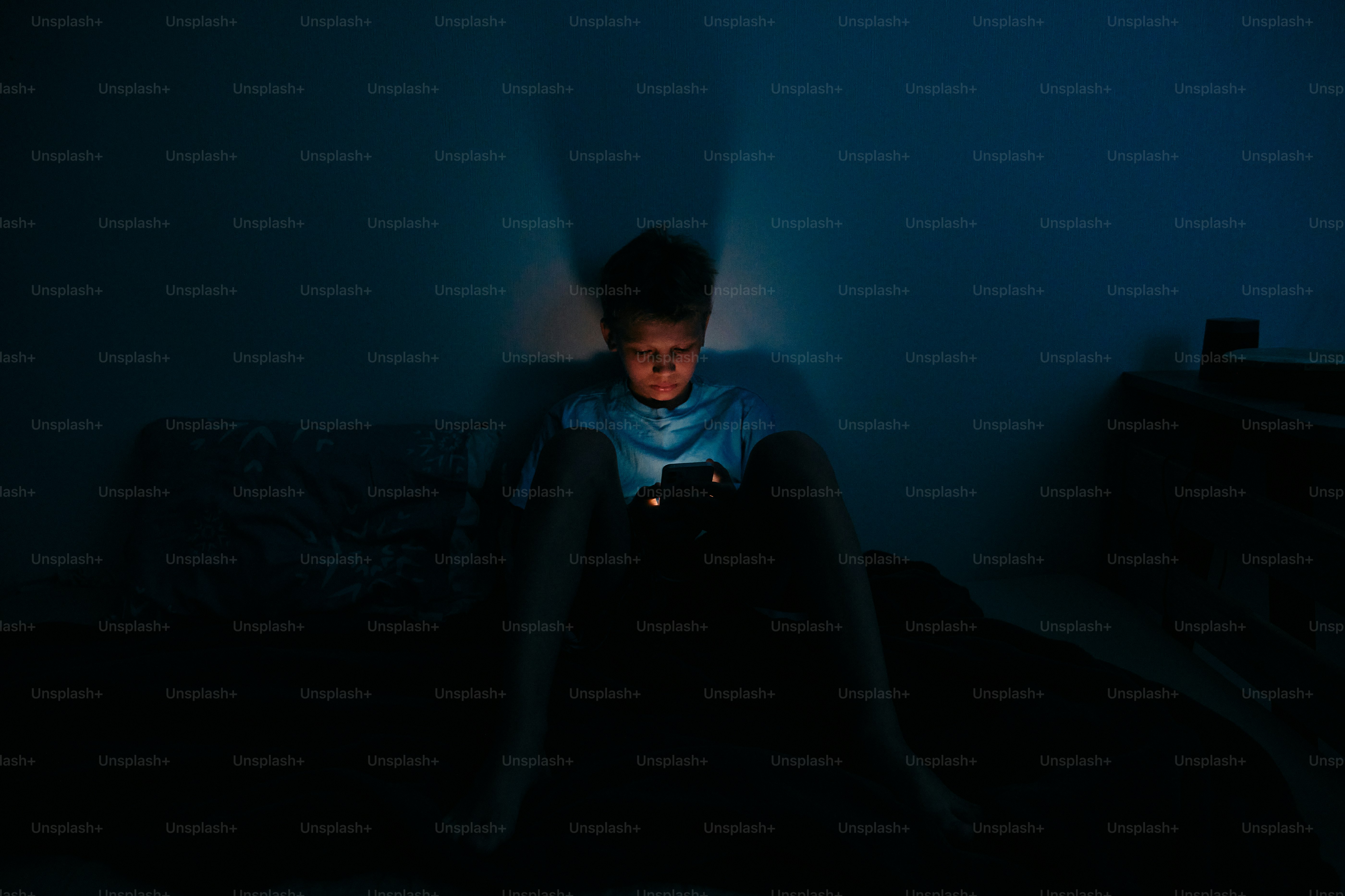 Young boy illuminated by phone screen in dark room photo – Technology ...