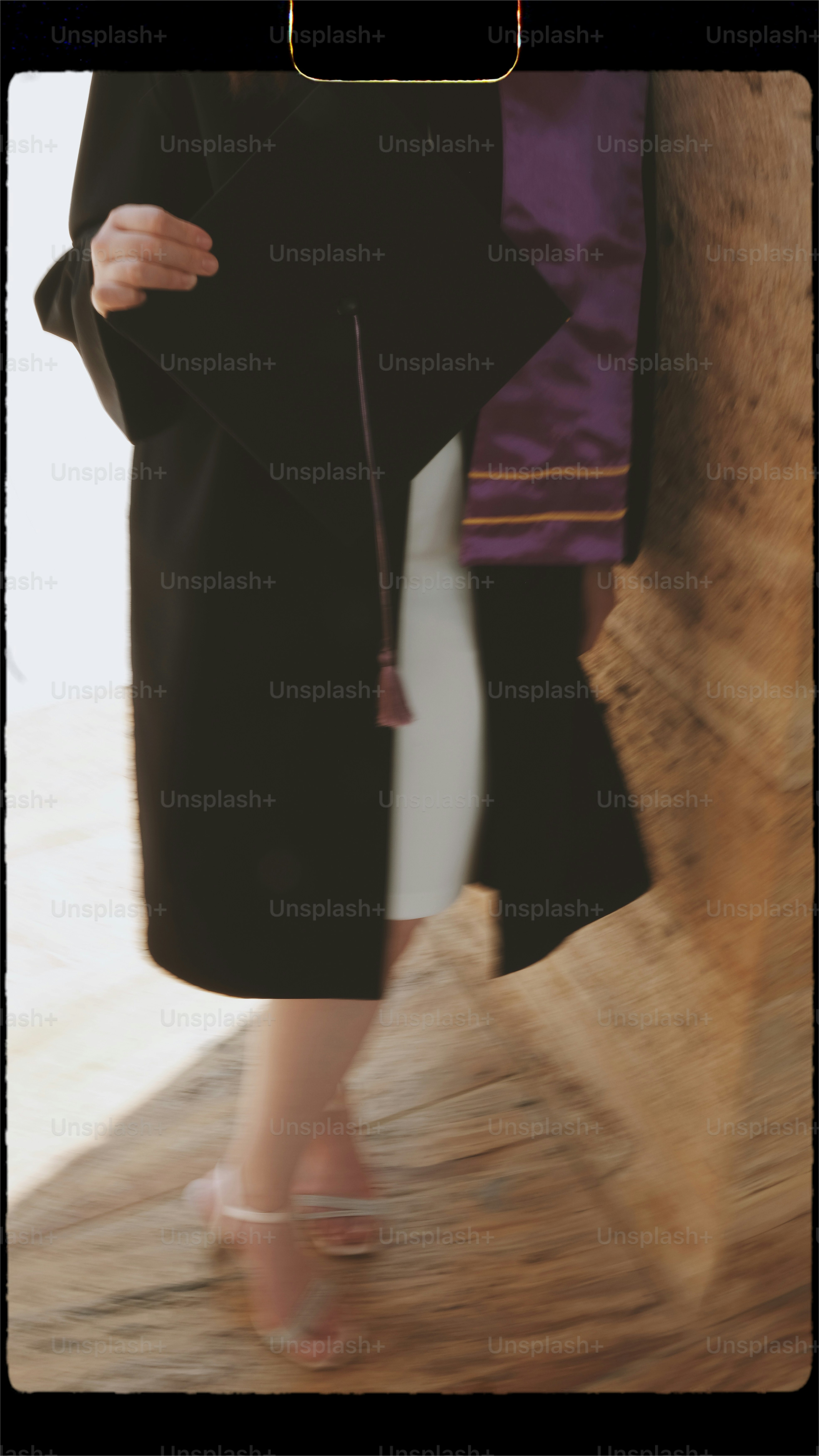 Graduate in cap and gown holds mortarboard, wearing sash.