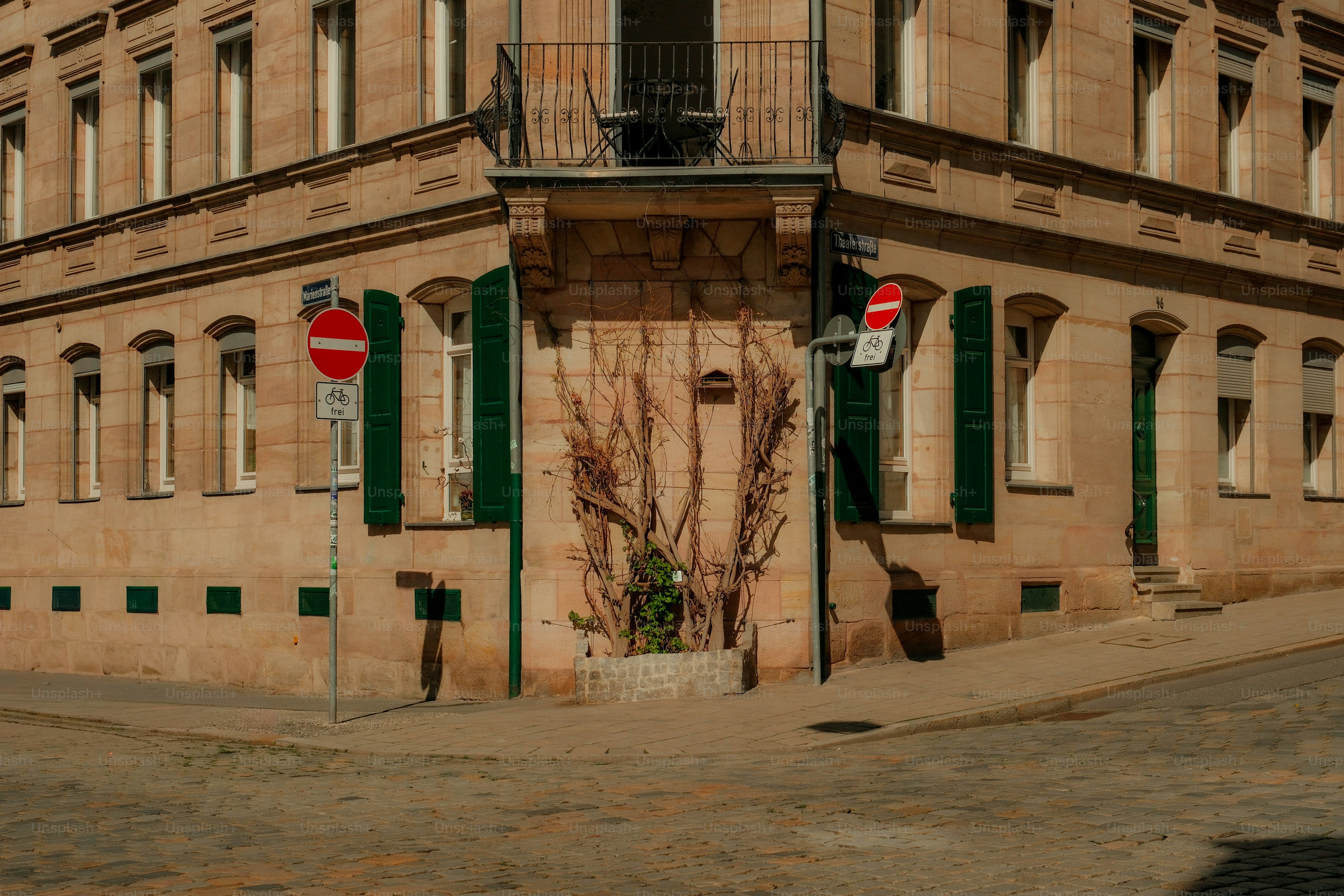Esquina de un edificio histórico con contraventanas y señales verdes.