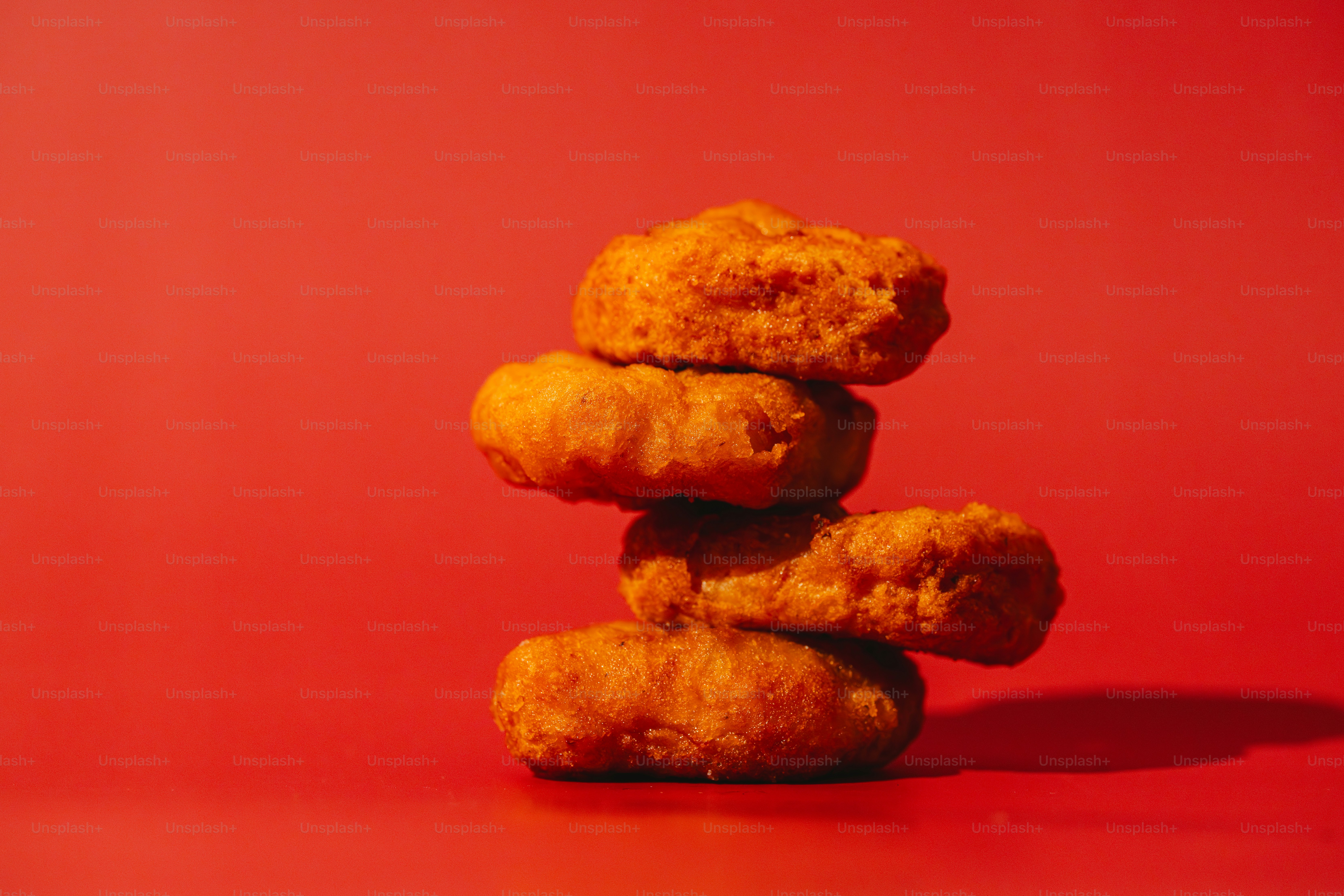 Stack of four golden chicken nuggets on red background