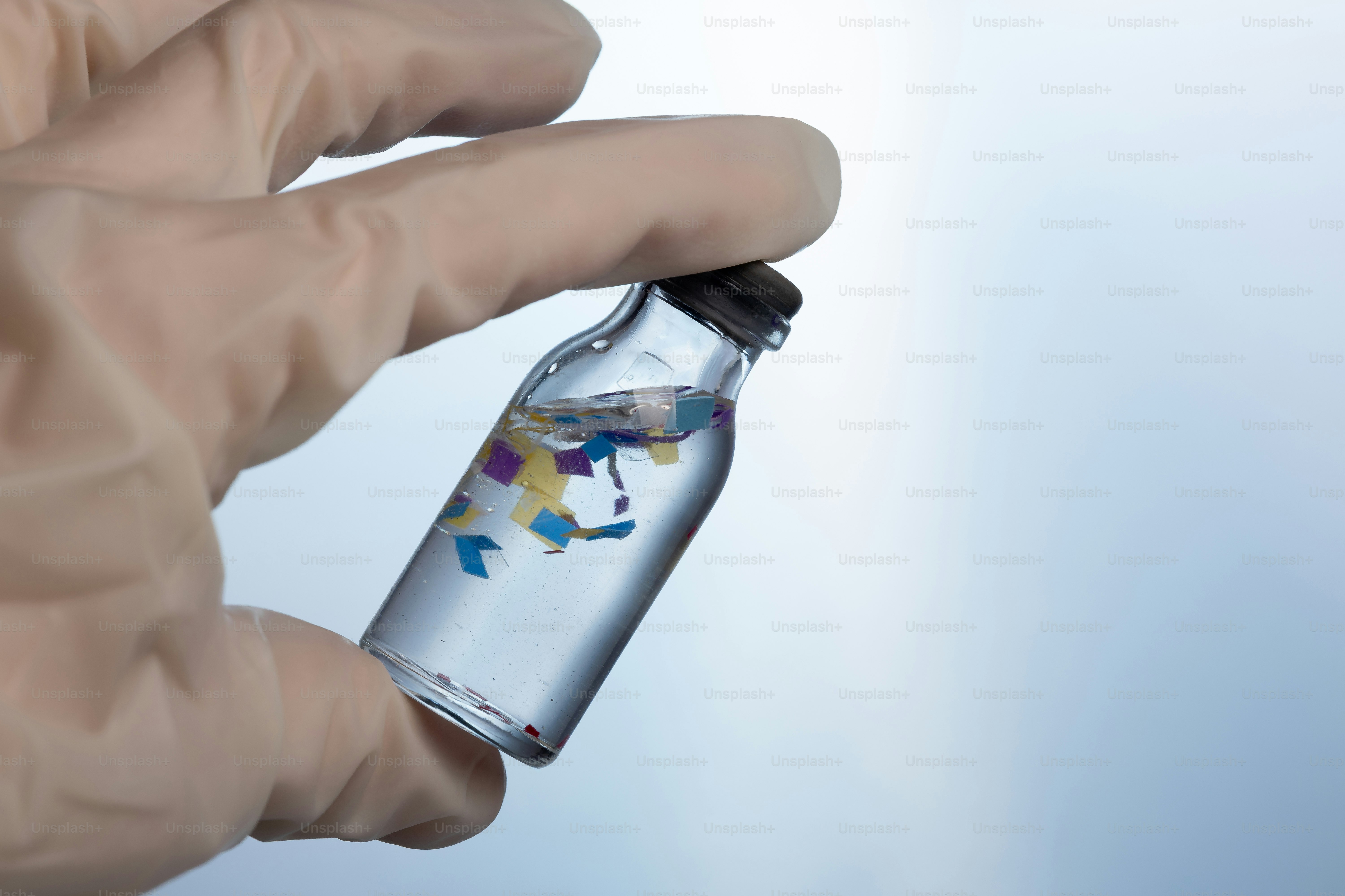 Hand holding vial with colorful microplastics in water