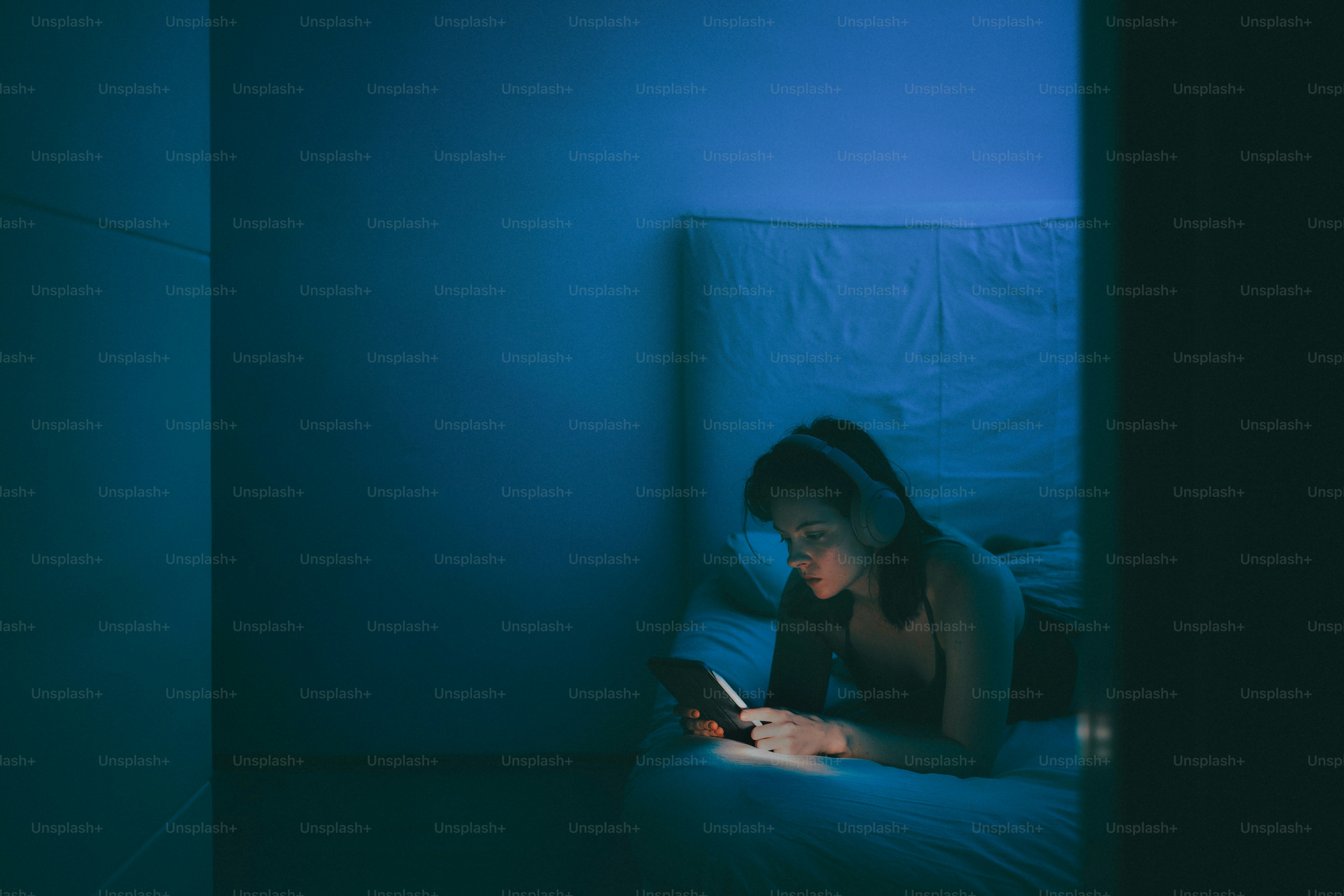 Woman in bed using phone with headphones on