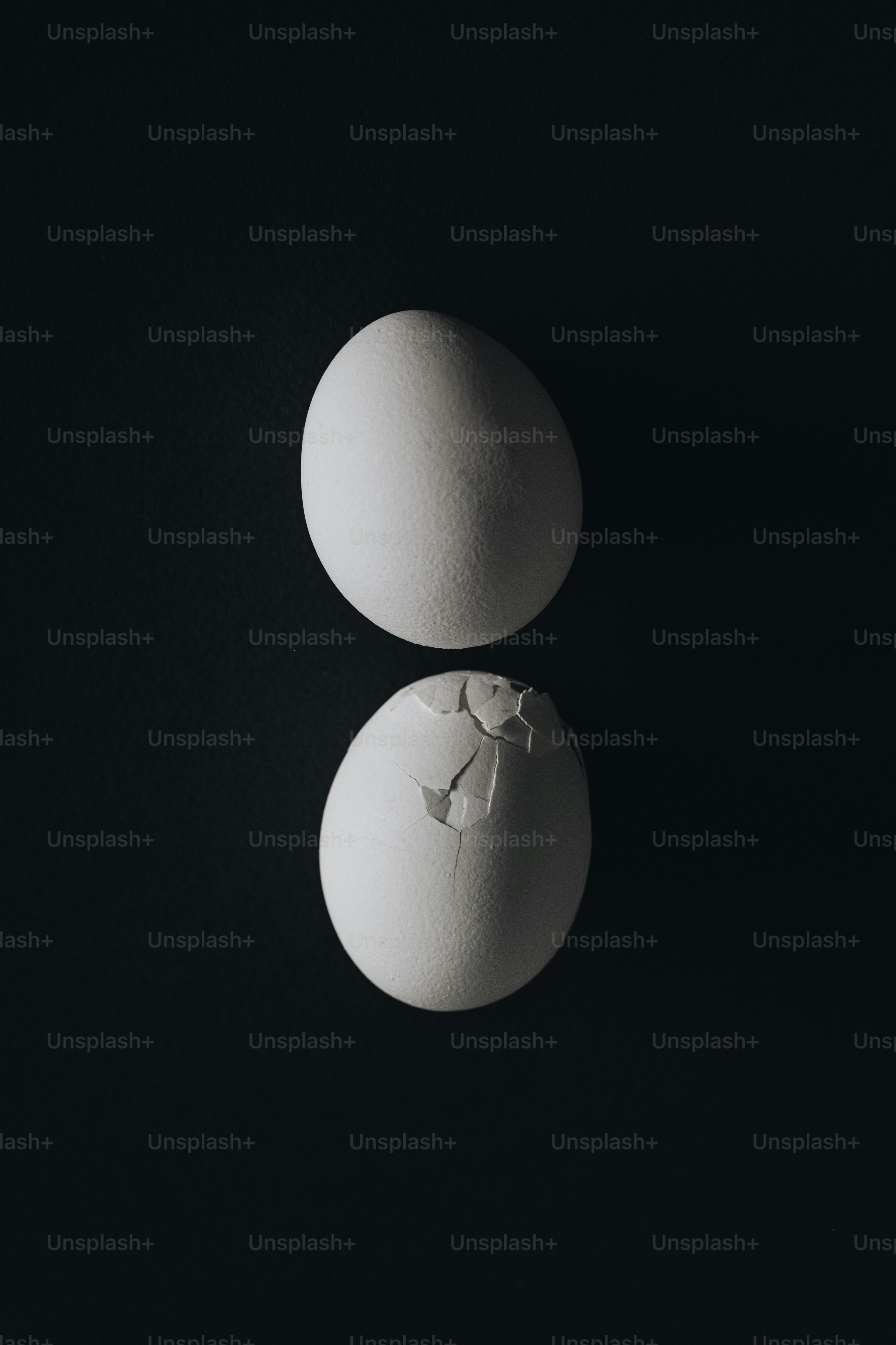 검은 배경에 흰 달걀 두 개, 하나는 깨진 달걀