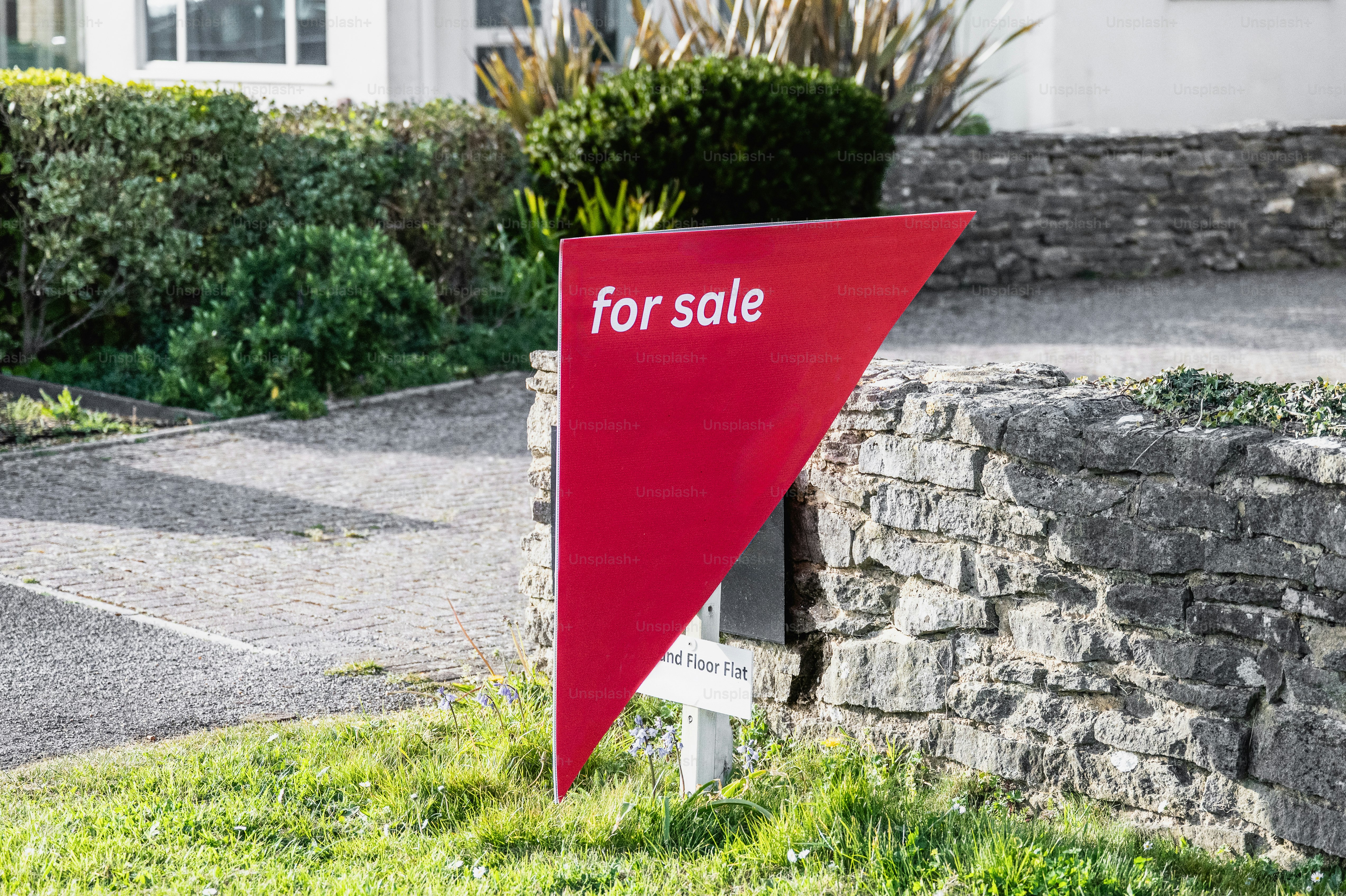 Panneau rouge à vendre devant un mur de pierre.