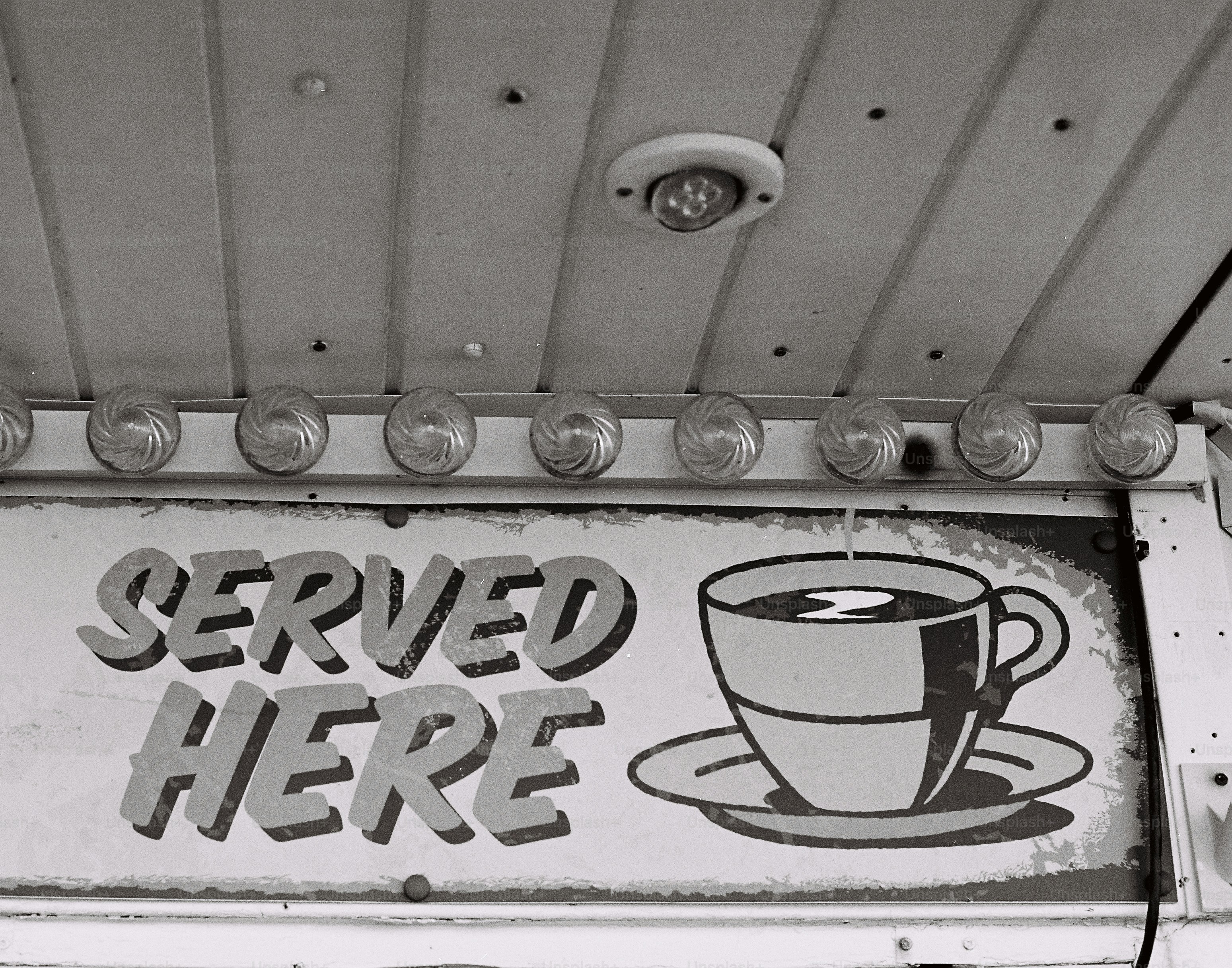 Sebuah tanda bertuliskan "disajikan di sini" dengan cangkir kopi.