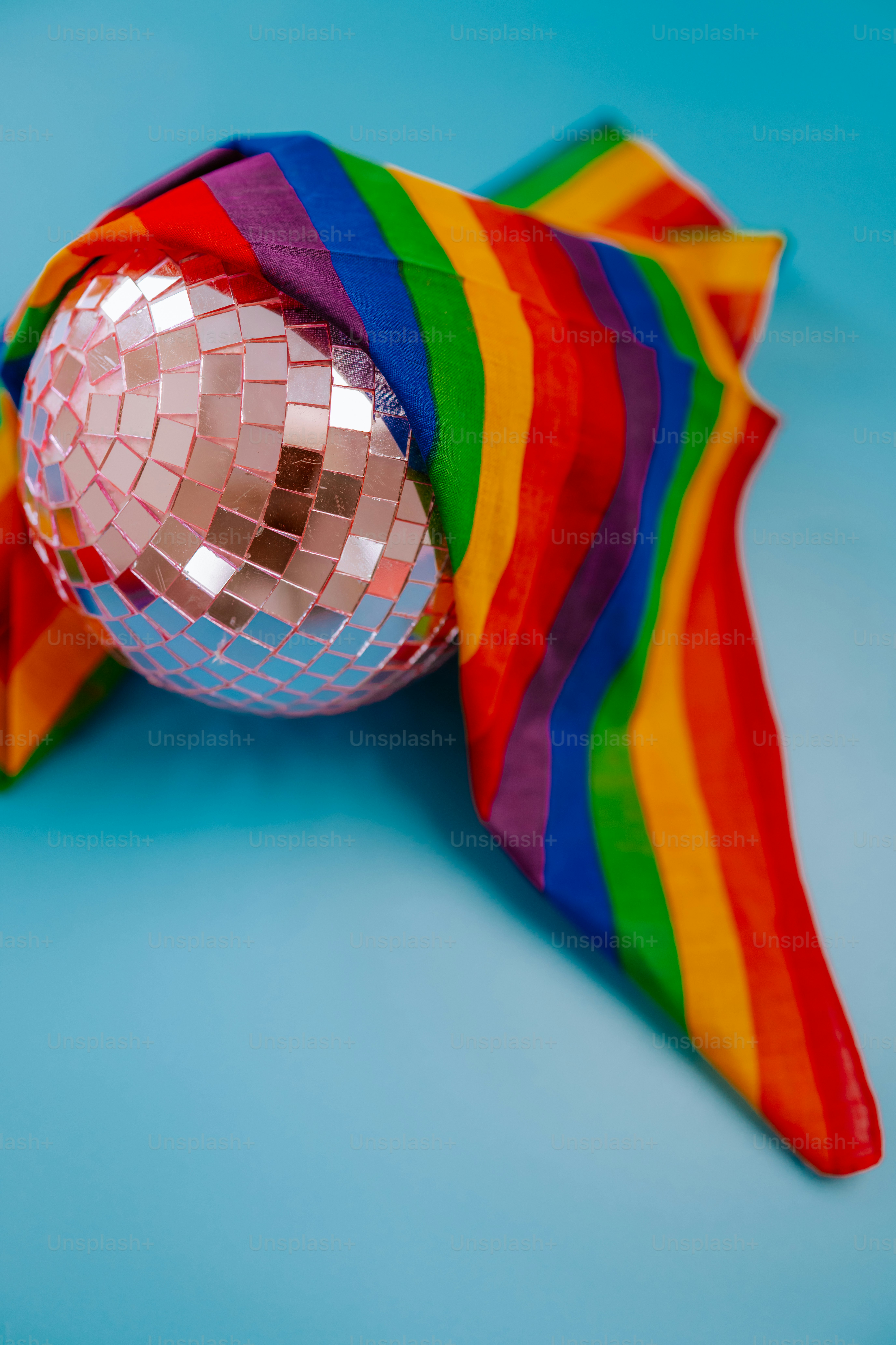 Disco ball draped with a rainbow flag on blue background