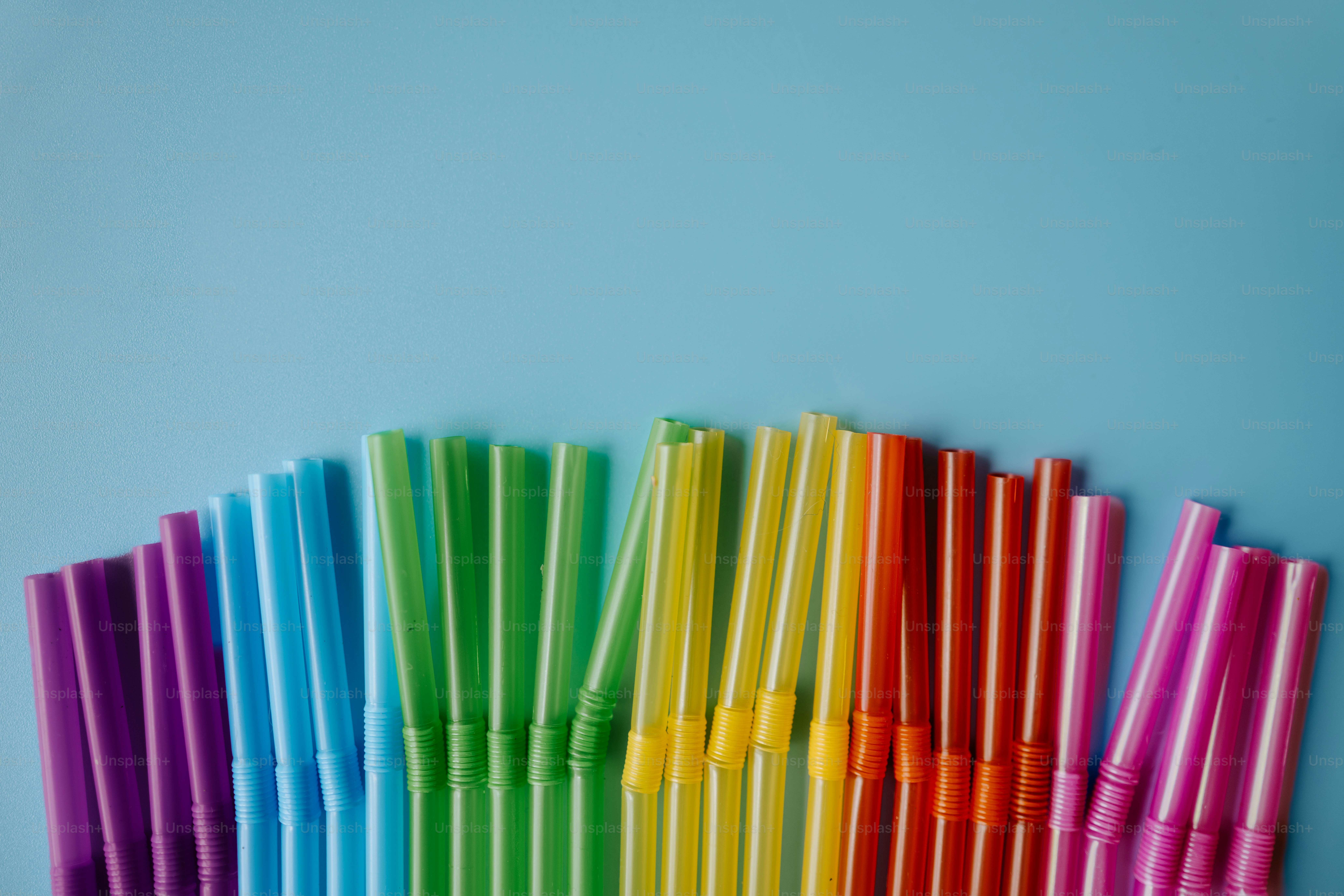 Pajitas coloridas dispuestas en un patrón de arcoíris sobre azul.