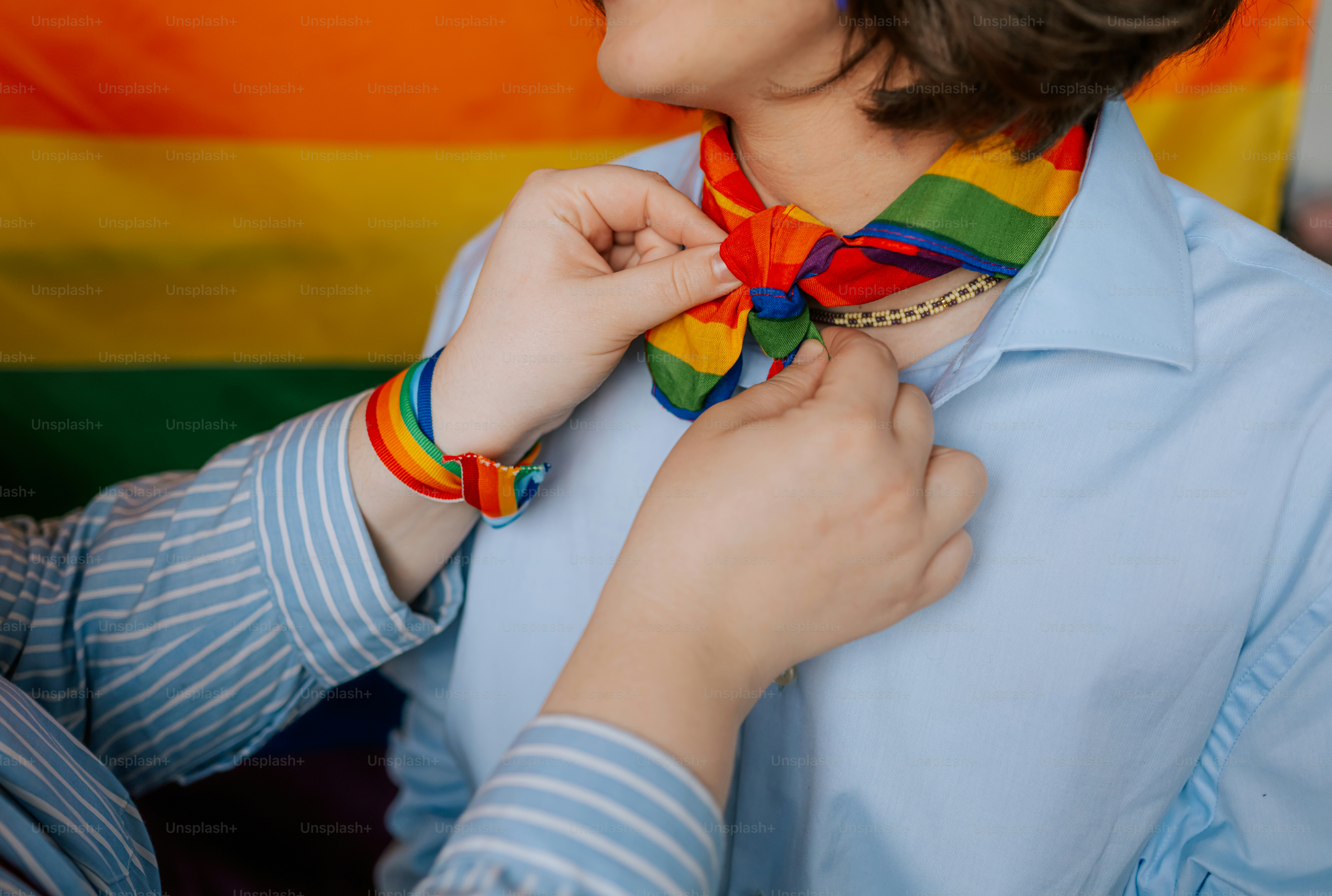Mani che legano una sciarpa arcobaleno a una persona.