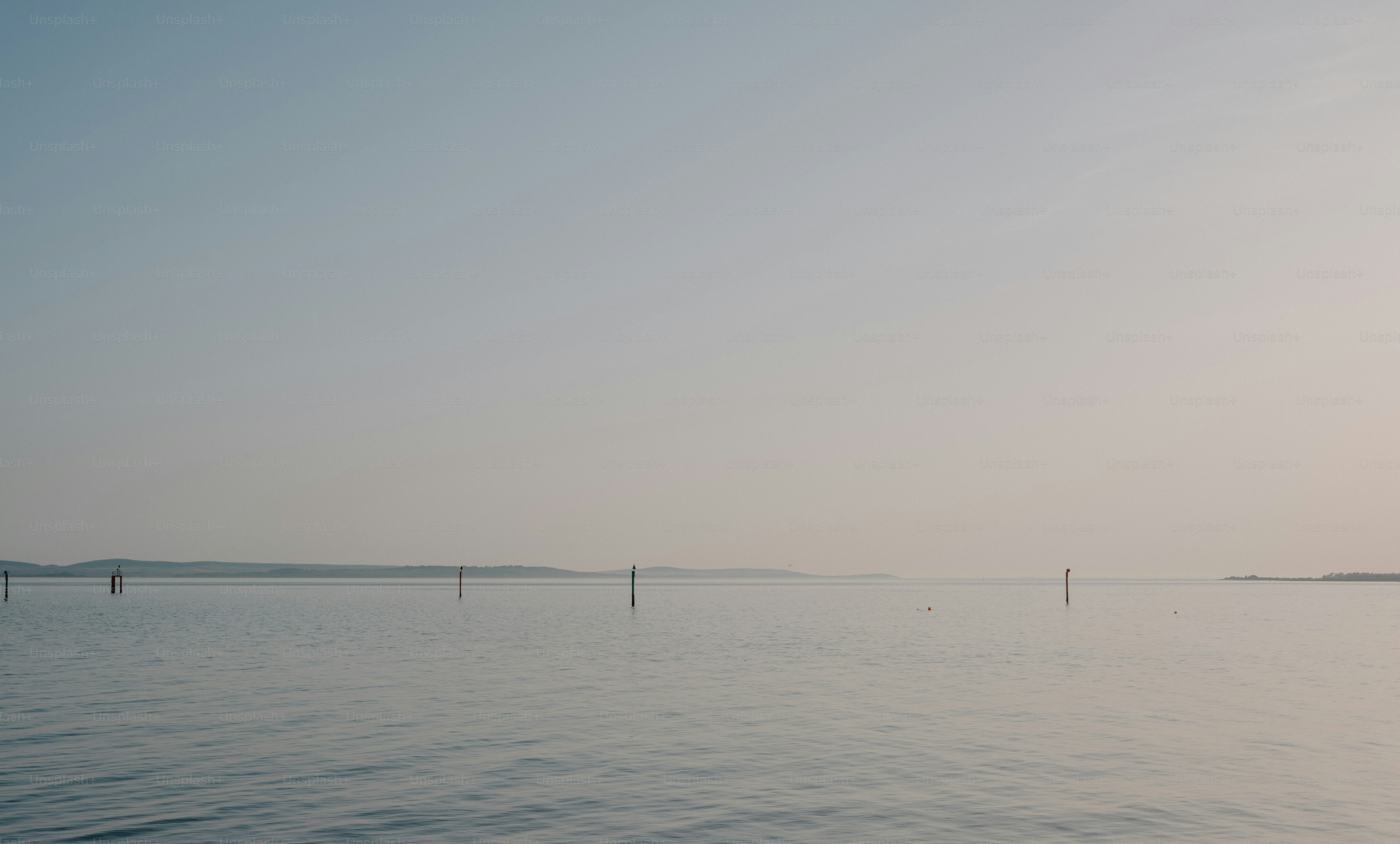 Calm ocean with distant poles at sunrise.