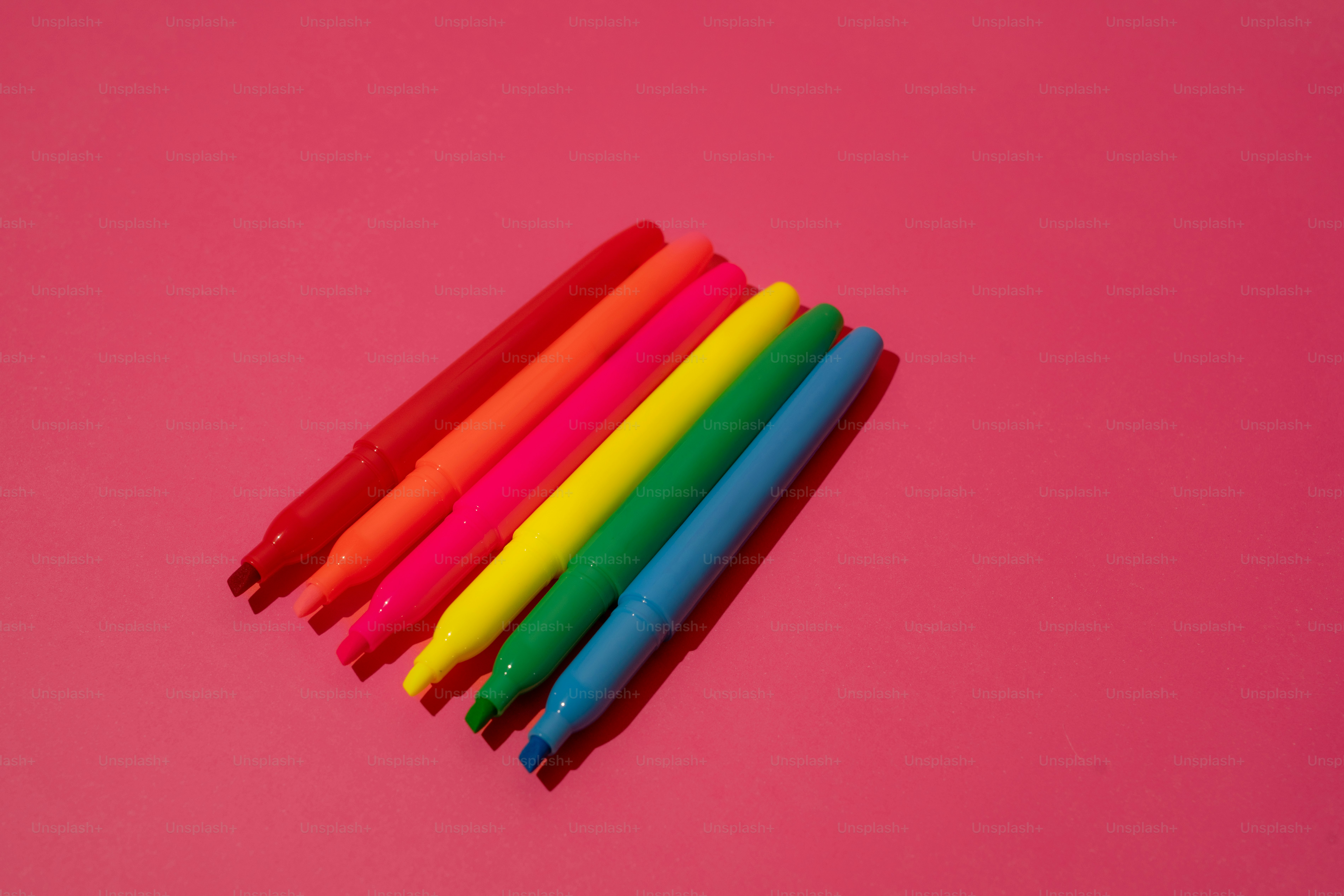 ピンクの背景にカラフルなマーカーが並べられています