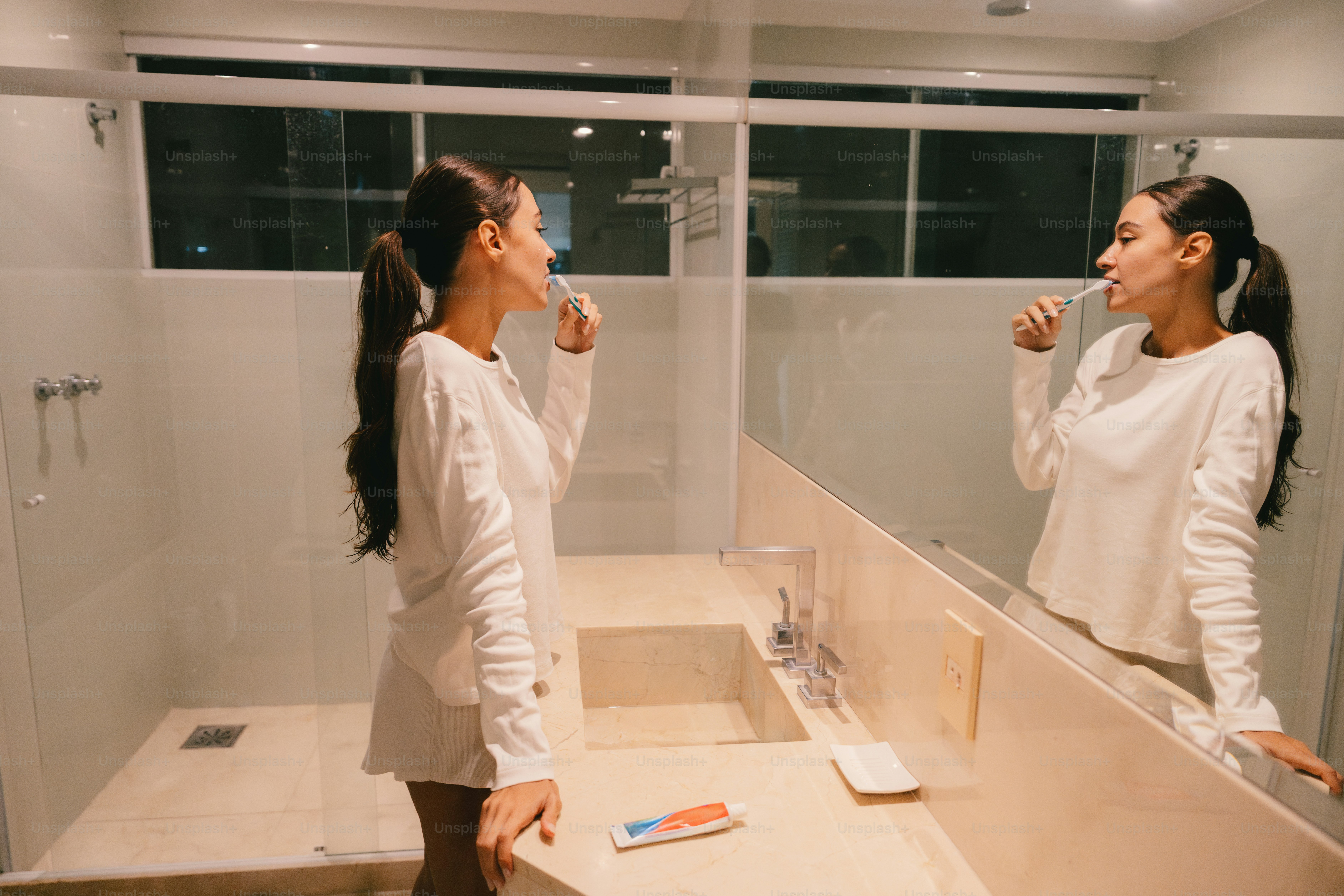 Mujer cepillándose los dientes delante del espejo del baño