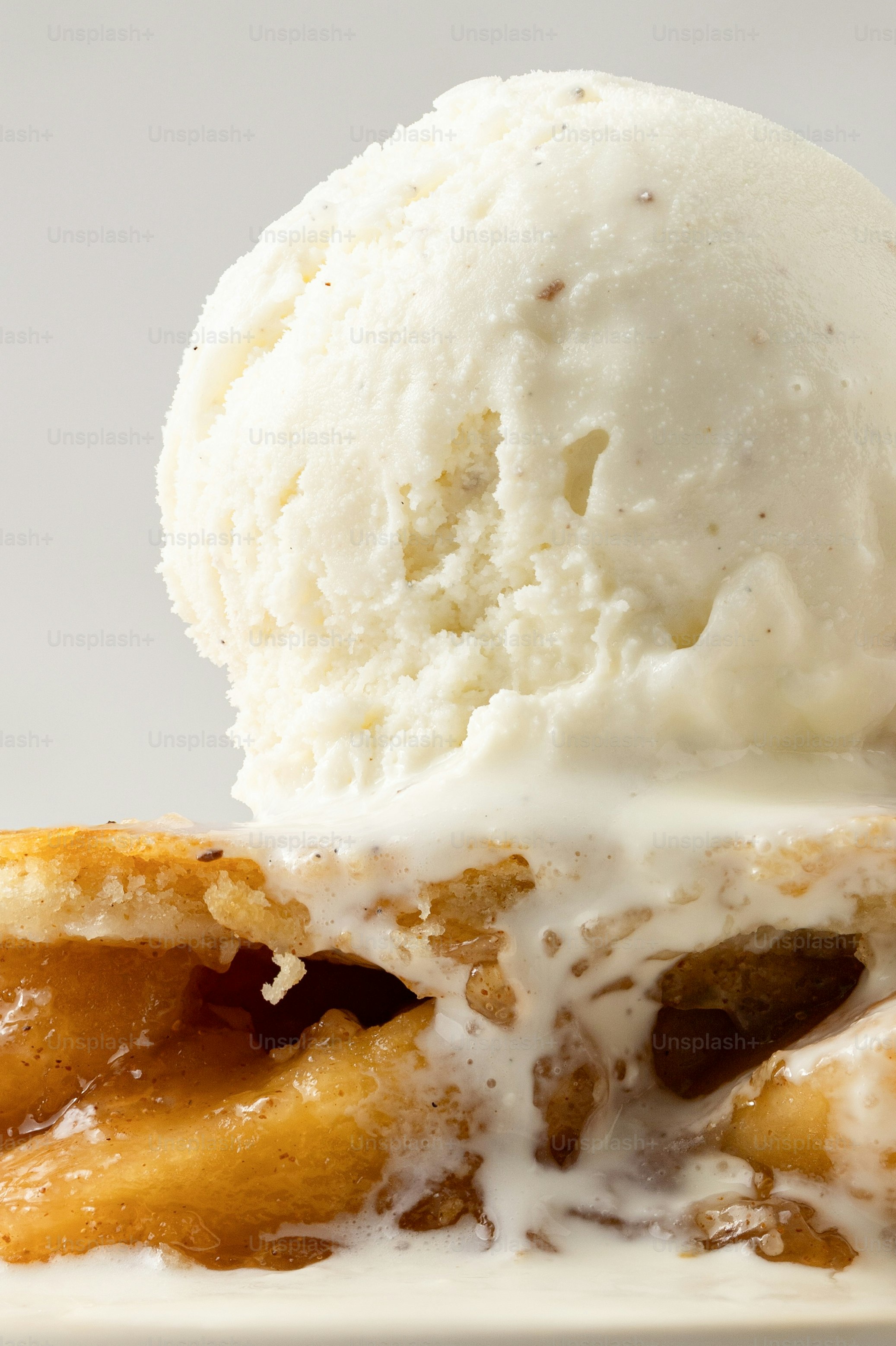 Scoop of vanilla ice cream melting over apple pie